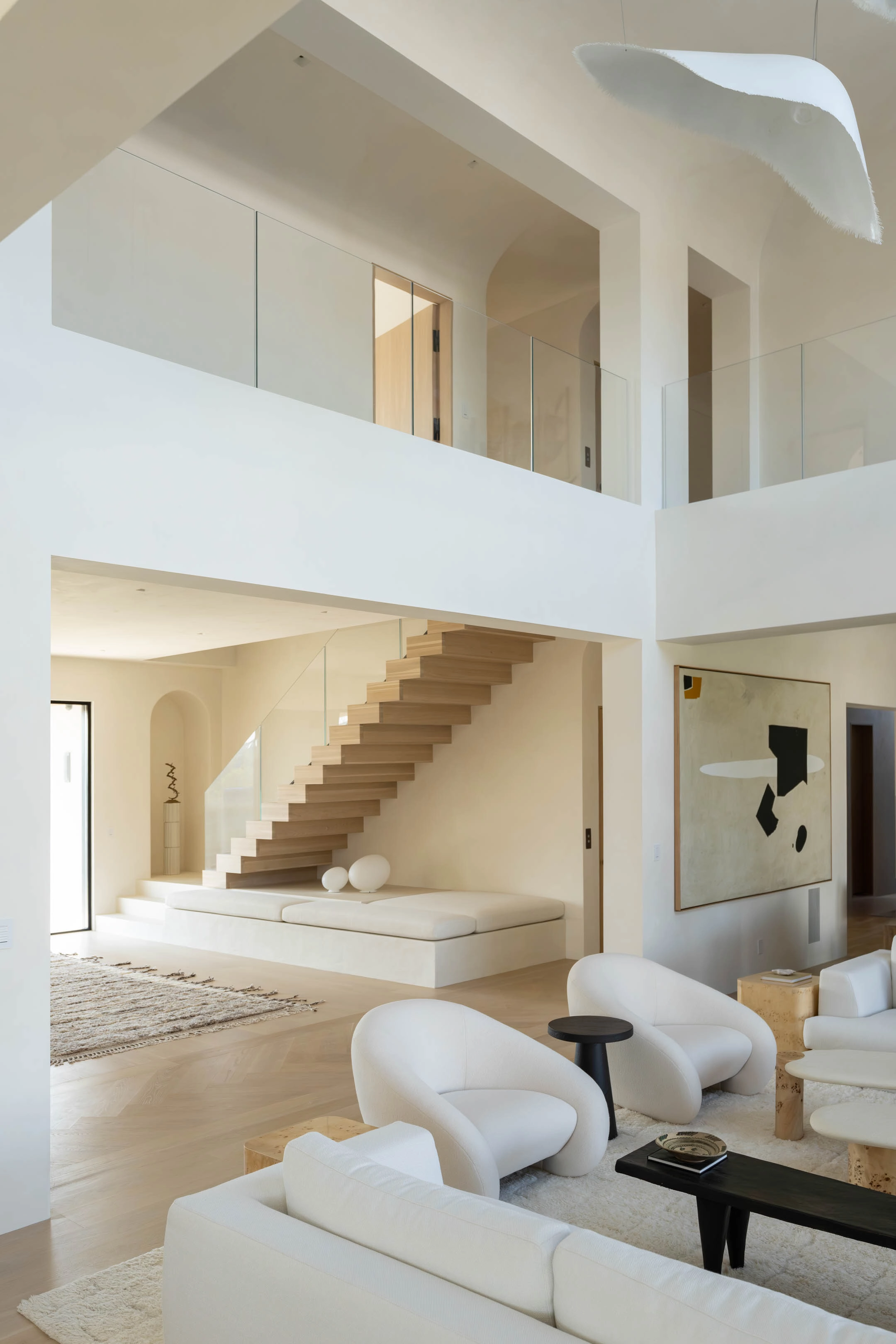 Double-height living room in pale plaster with the stair rising at the far wall