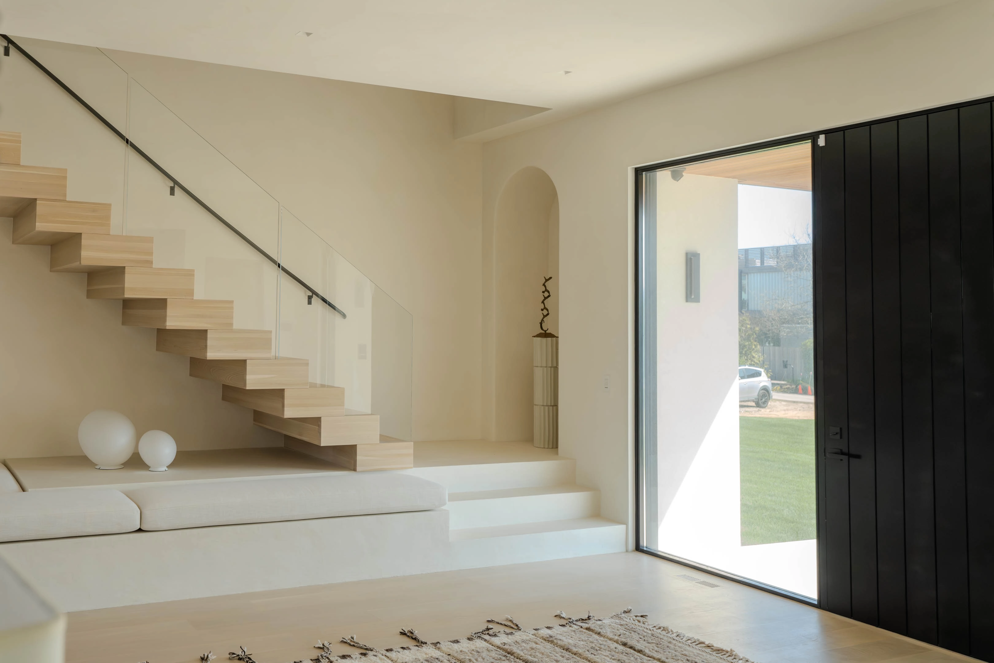 Stair at left beside a black pivot door opening to the garden