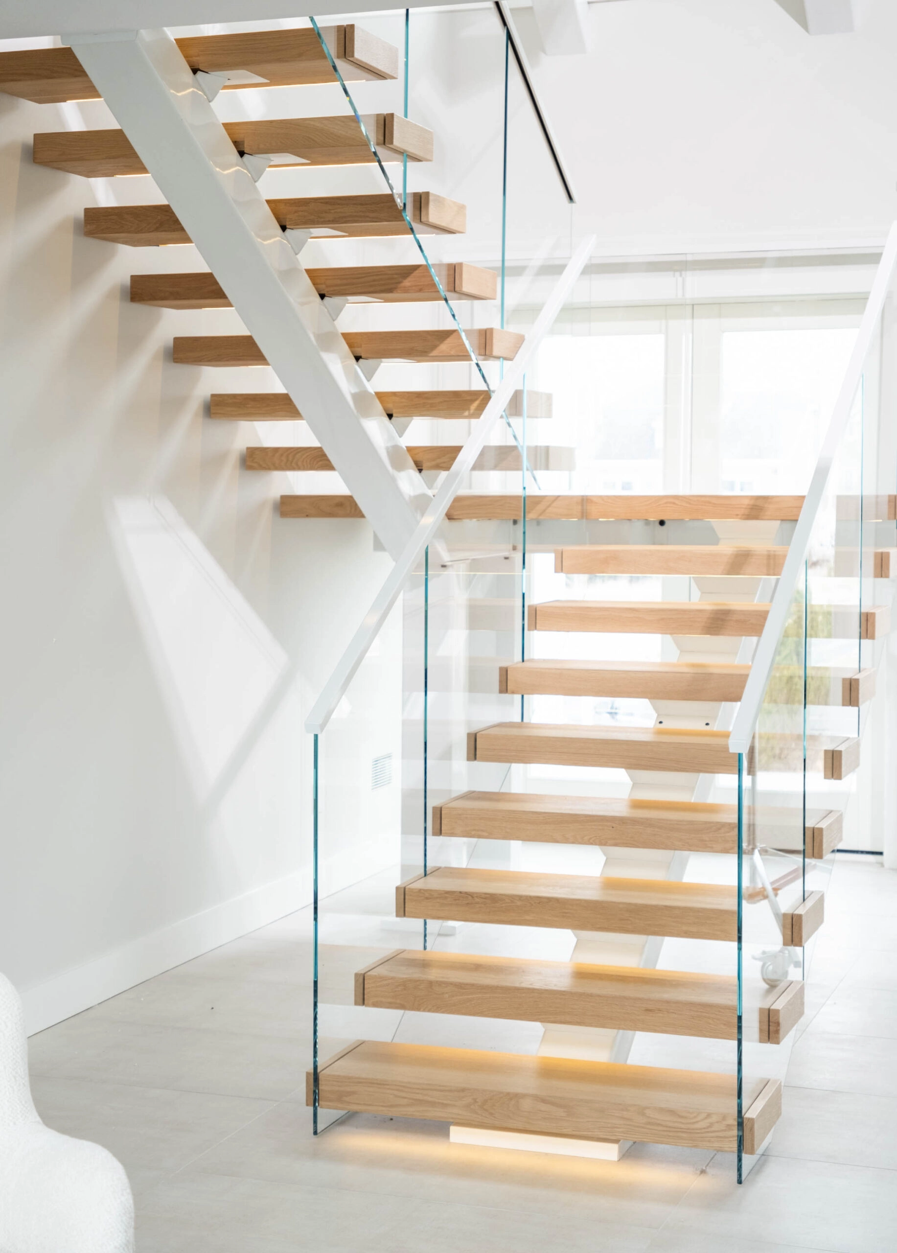 White center stringer carrying pale wood treads with glass railing and a lit bottom step