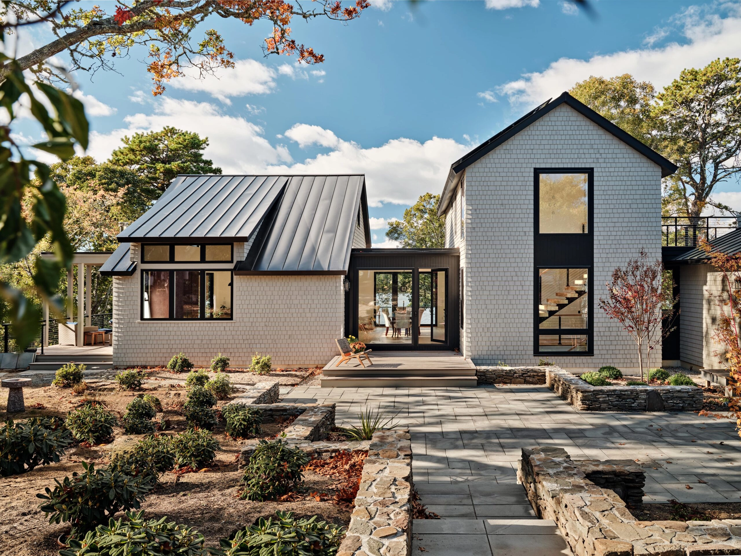 White brick home with a standing-seam roof above terraced stone landscaping
