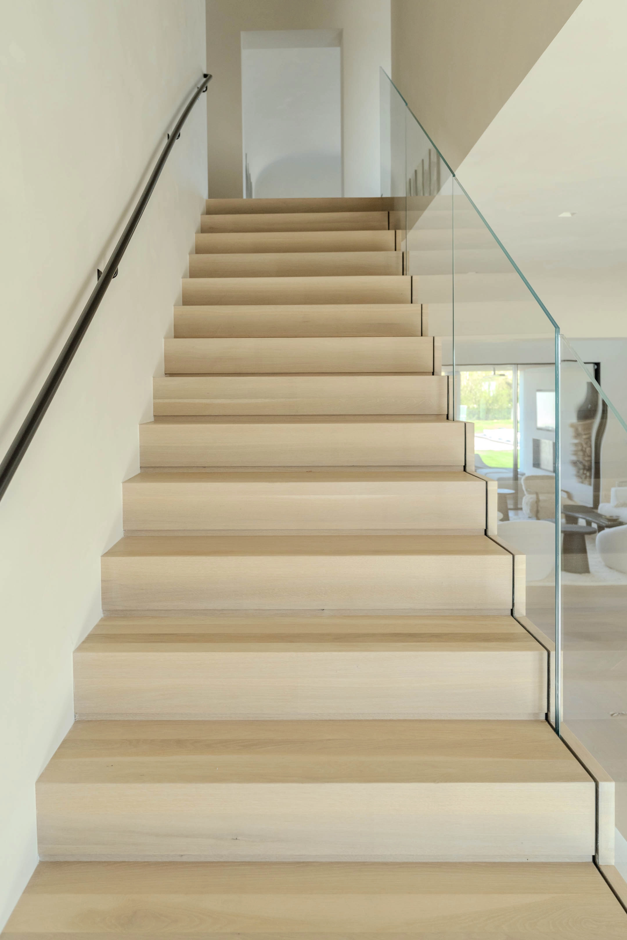 View up a straight flight with wall handrail on one side, glass on the other