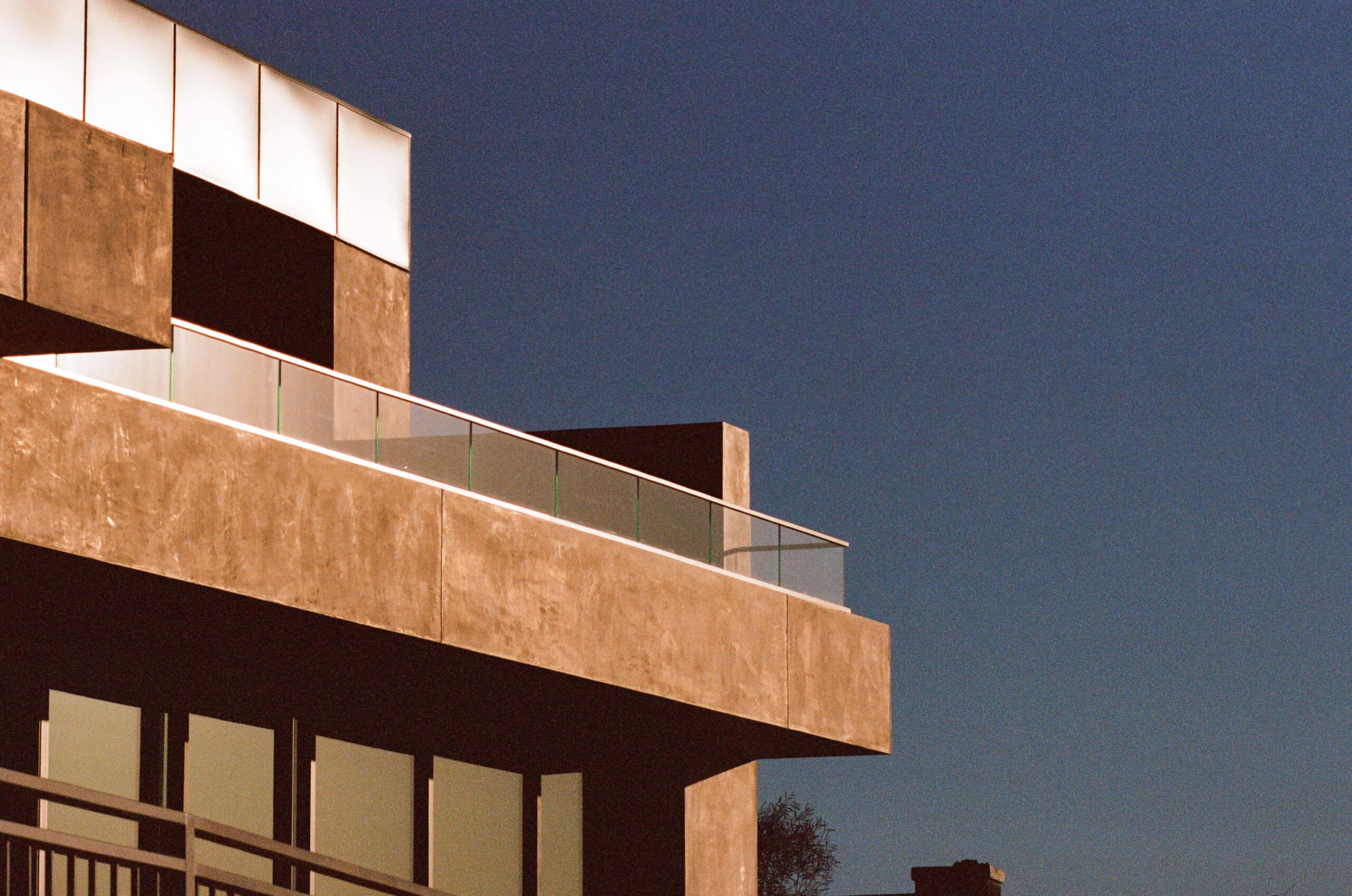Stucco upper level edged with glass railing against deep blue evening sky