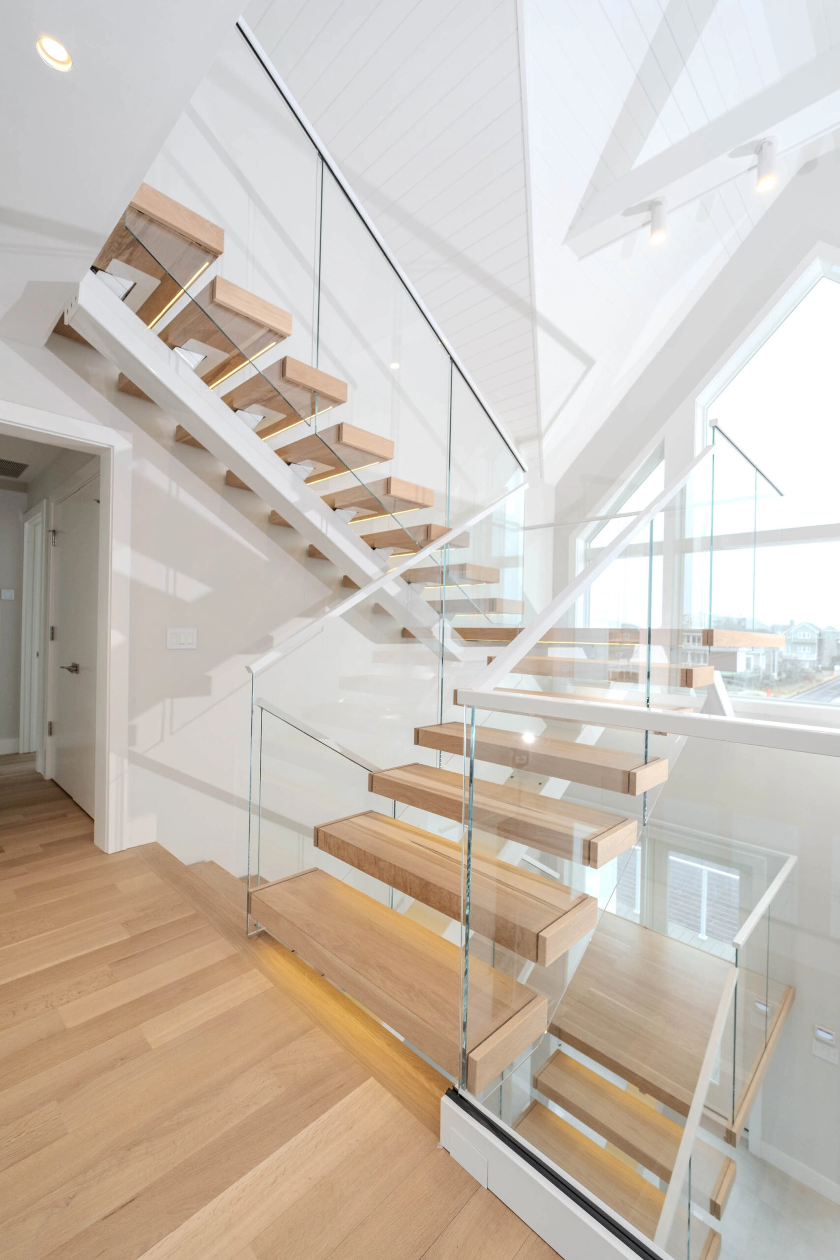 Stair seen from the landing below with glass railing under a white paneled ceiling