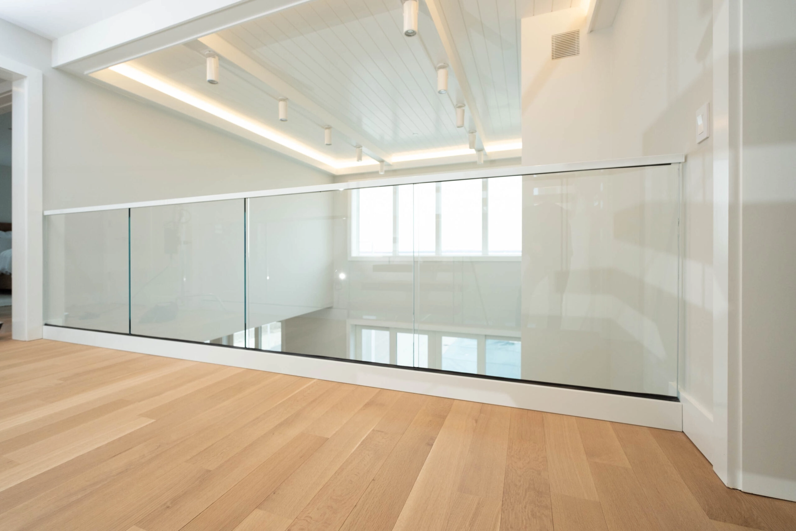 Balcony glass railing running the hallway edge above plank flooring and a vaulted ceiling