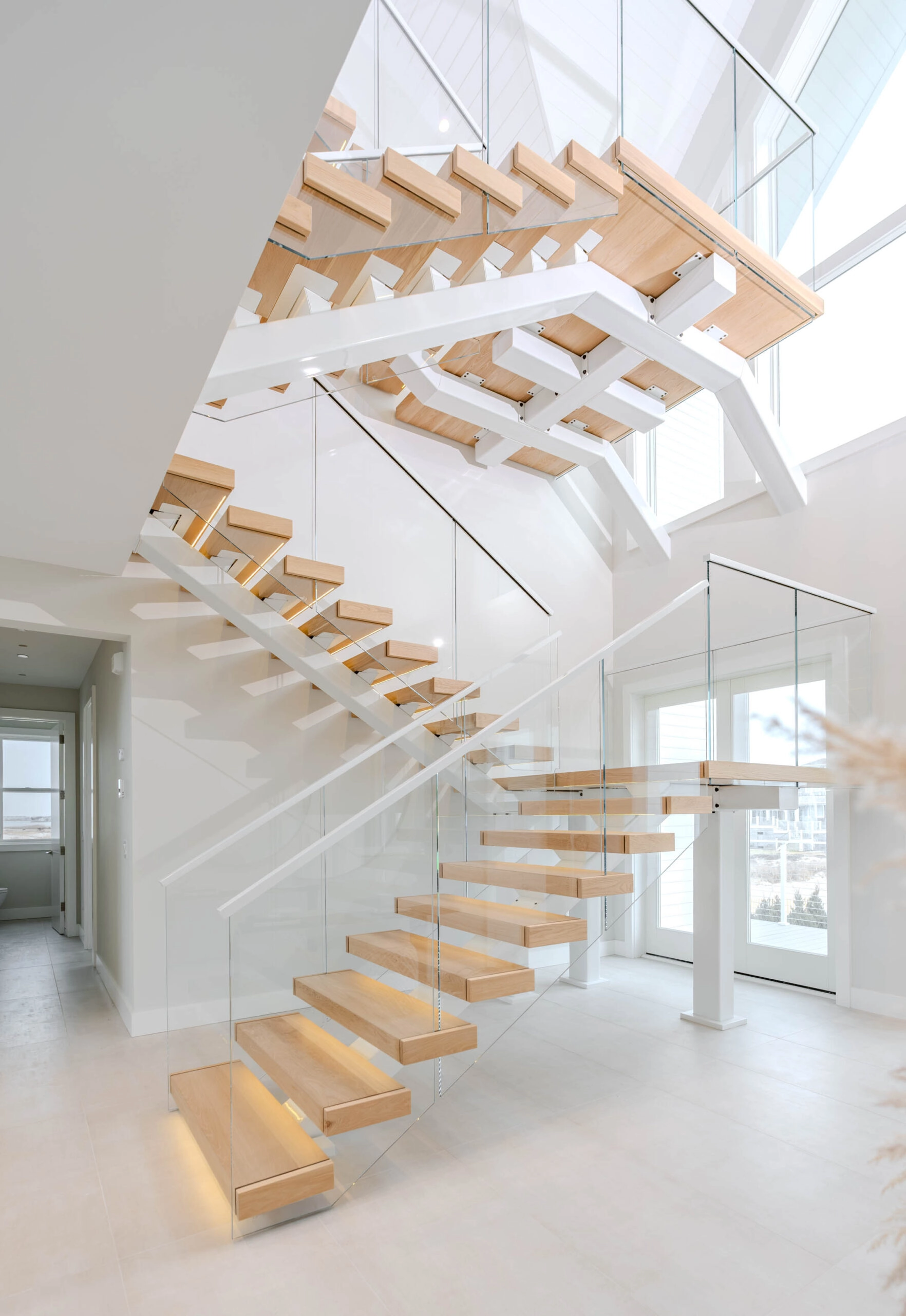 Three flights stacked in a bright stairwell on white stringers with glass railing