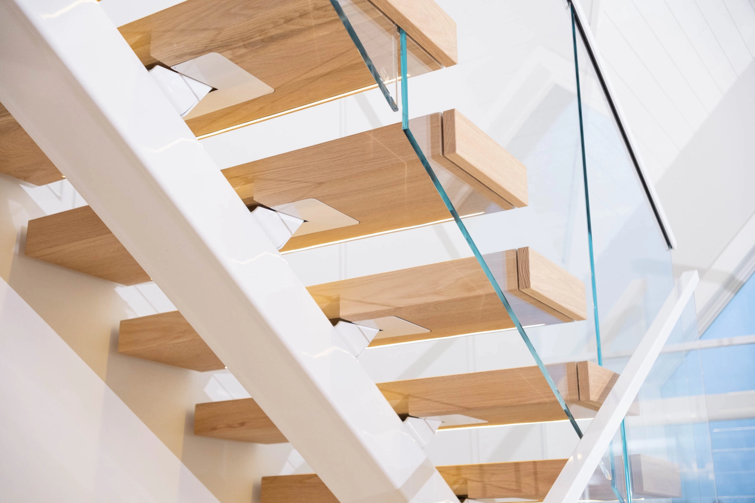 Looking up at cantilevered treads and clear glass panels along the white stringer