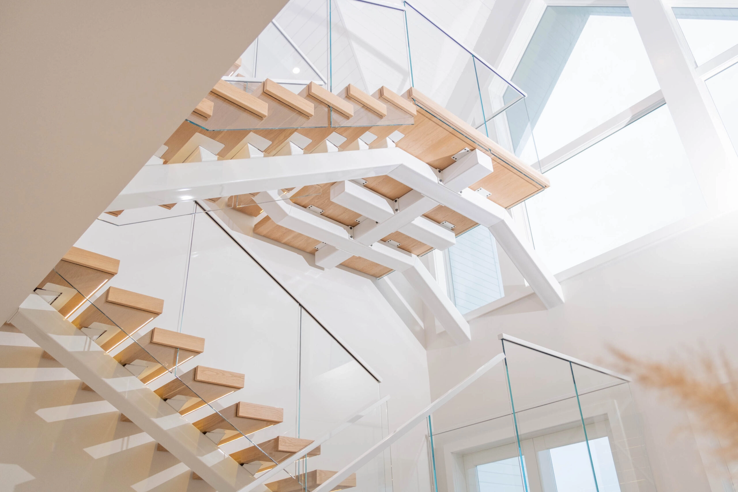 Upward view of stacked flights and glass railings toward a bright angled skylight