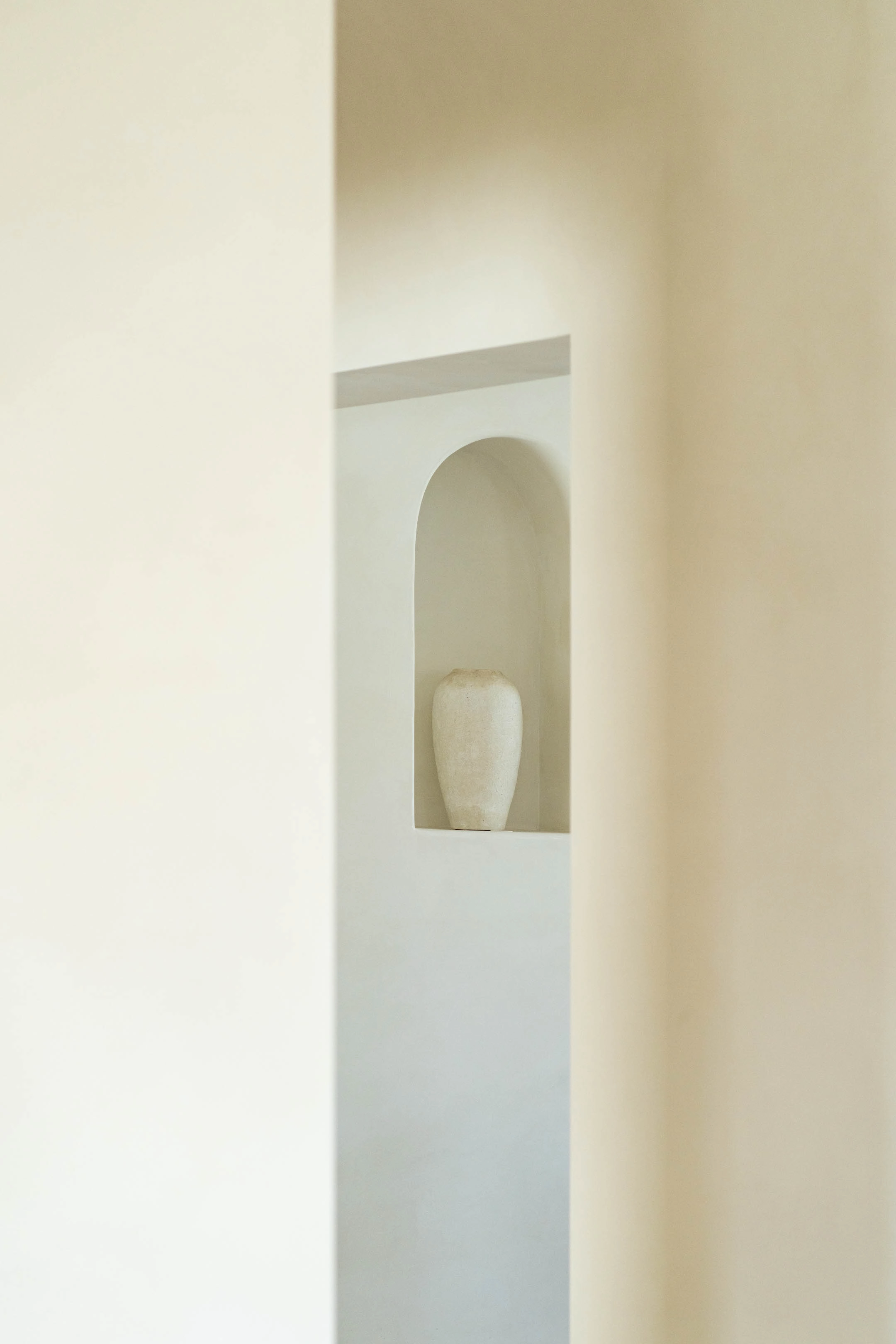 Plaster passage framing a lit arched niche holding a pale vessel
