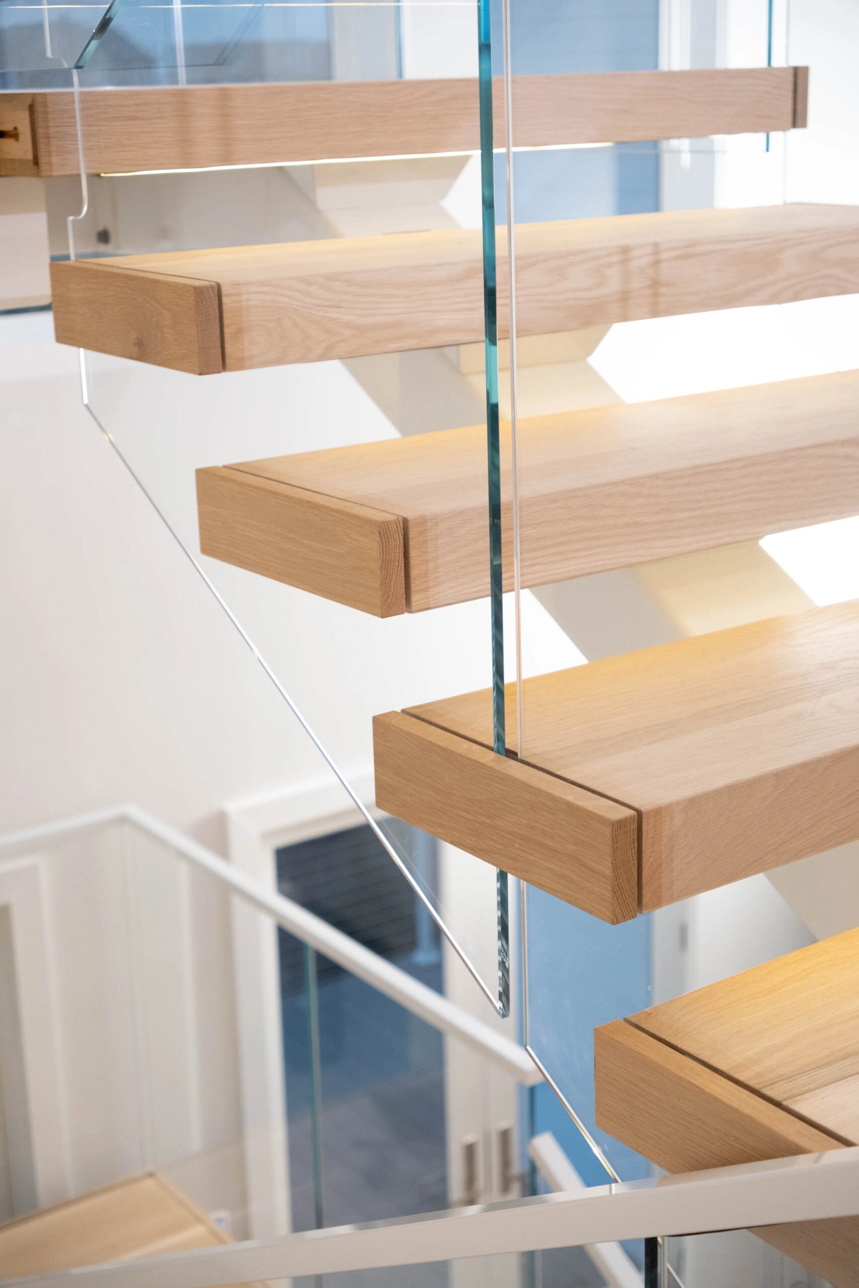 Close view of thick wood treads cantilevered from the white stringer beside glass
