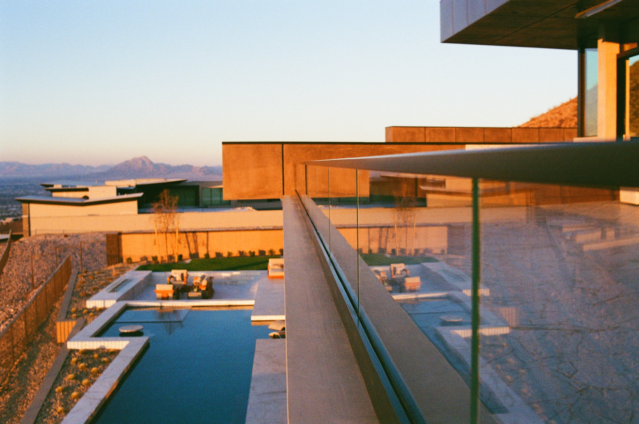 Long pool and terraces at sunset seen past a glass railing panel