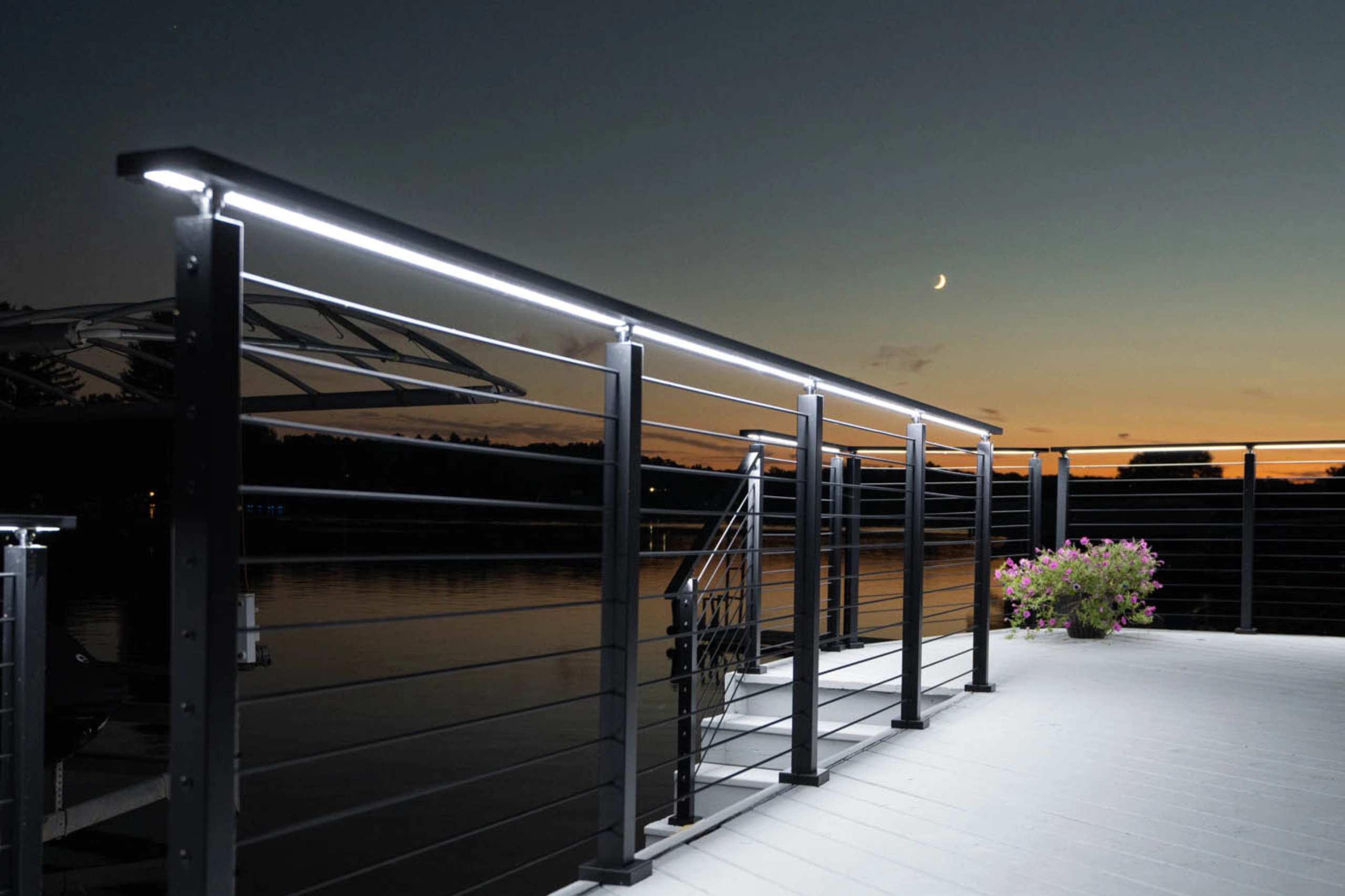 Lit top rail glowing along the deck edge at dusk beneath a crescent moon