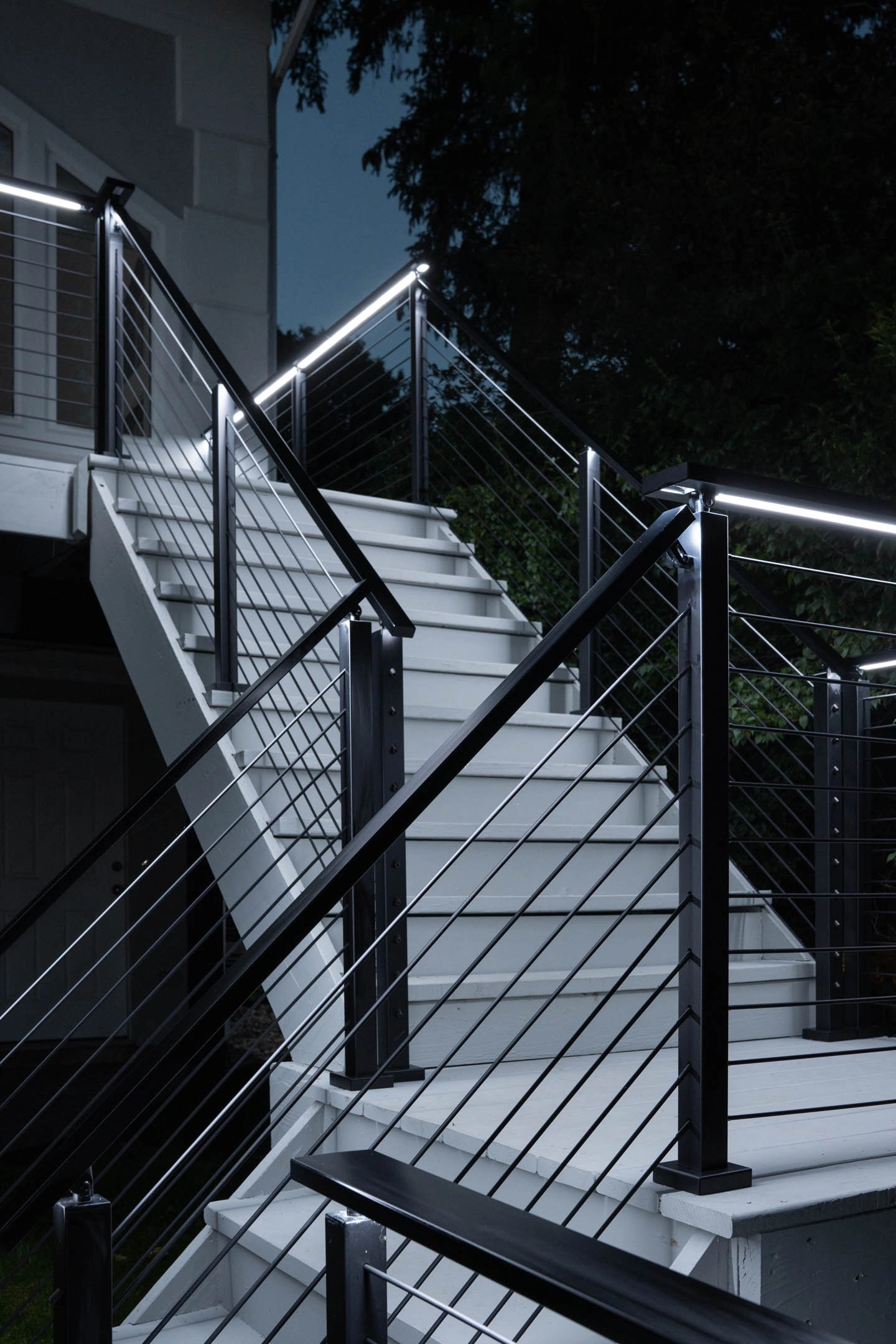 Stairs at night with lit handrails washing light across the pale treads