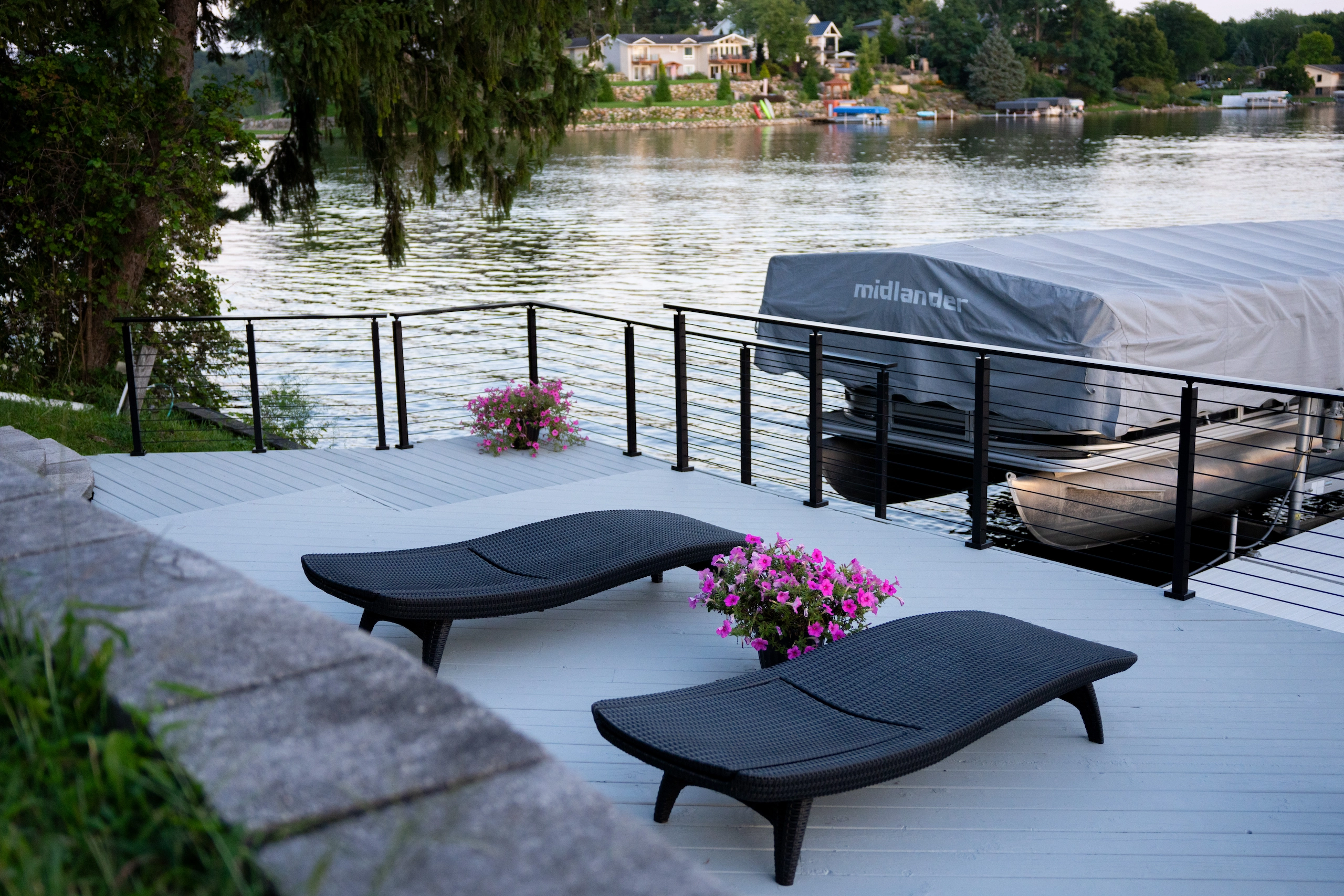 Lakeside deck with black rod railing, loungers and a covered boat lift beyond