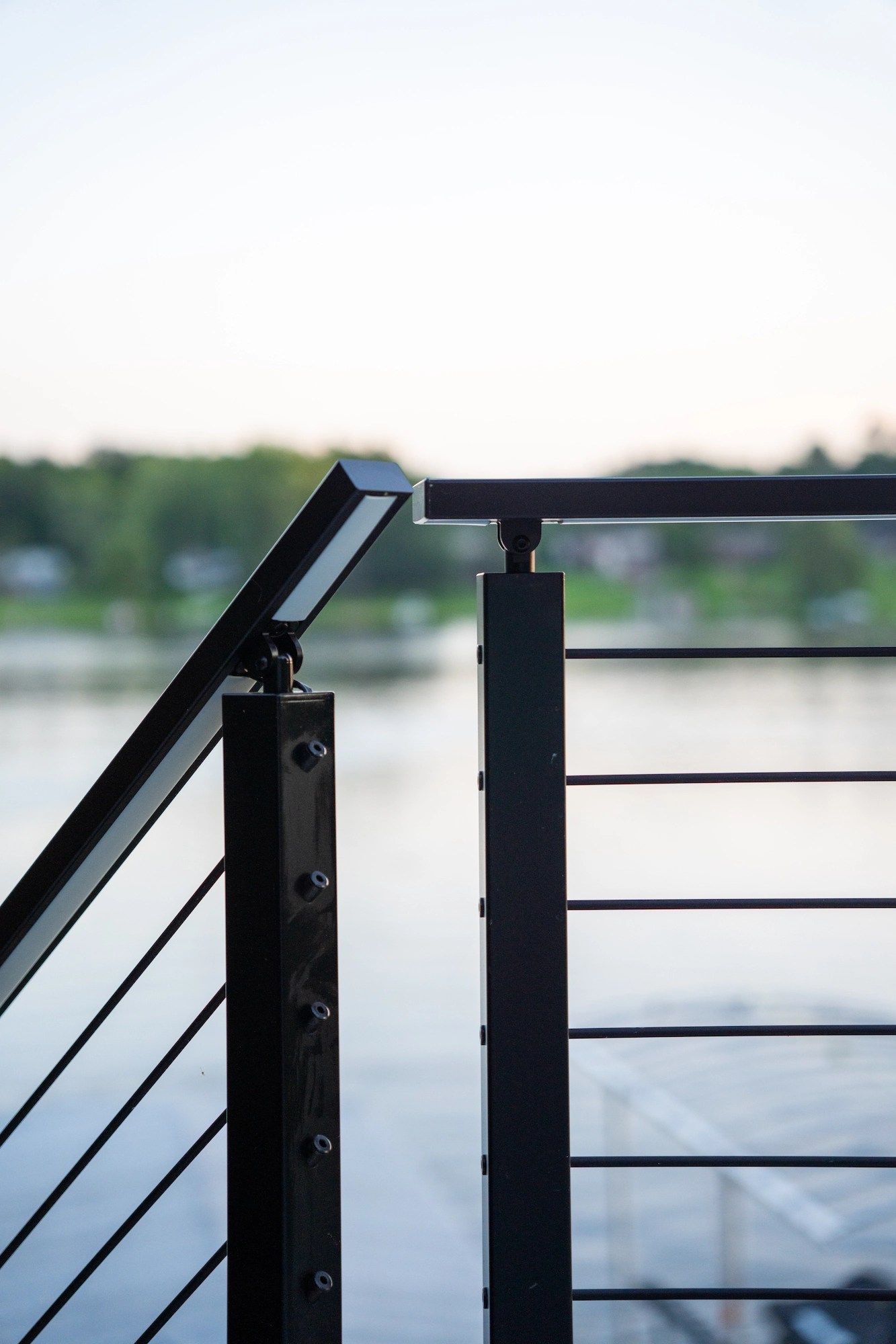 Close view of a black post and top rail against still lake water
