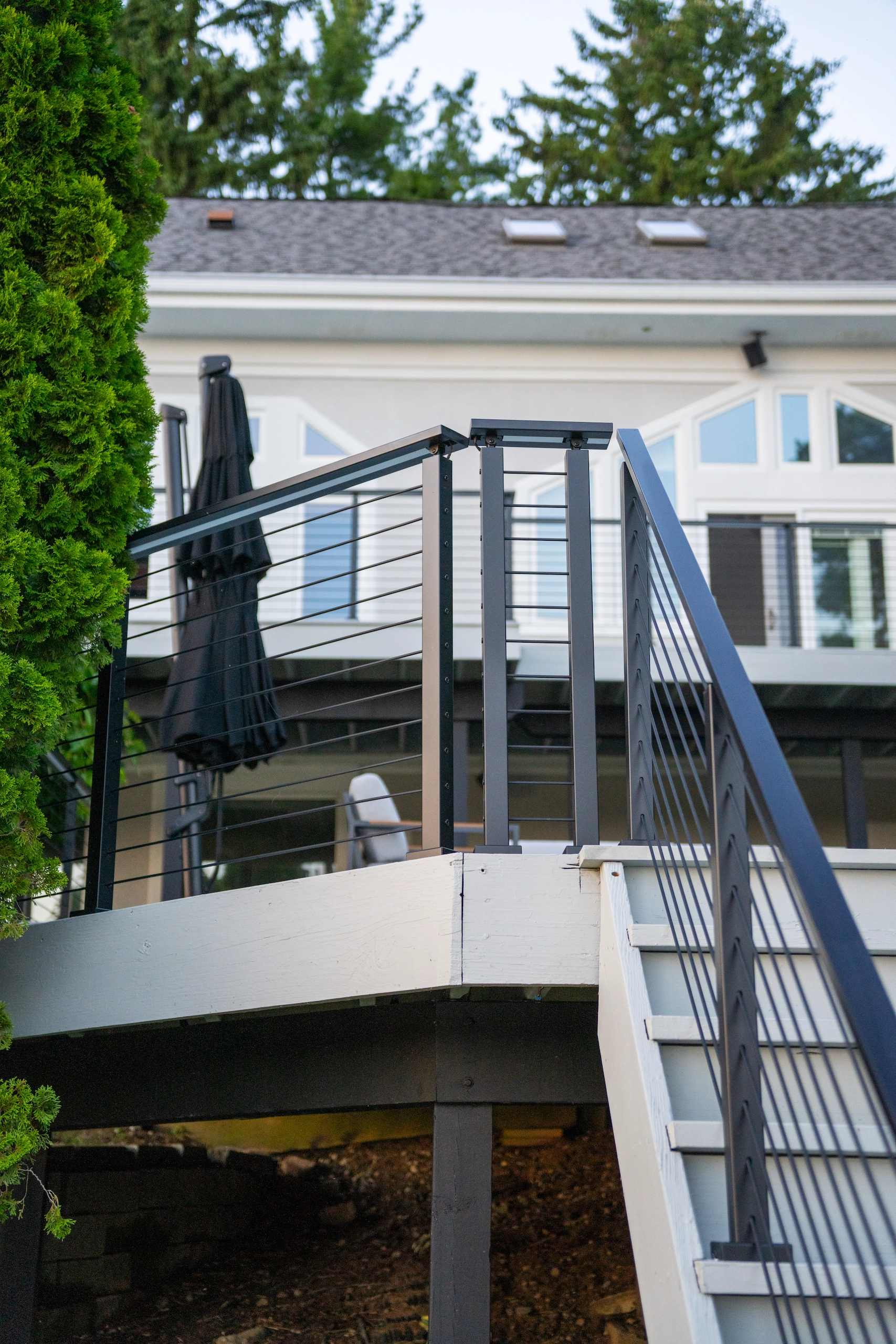 White house with a raised deck and black rod railing above a curved stair