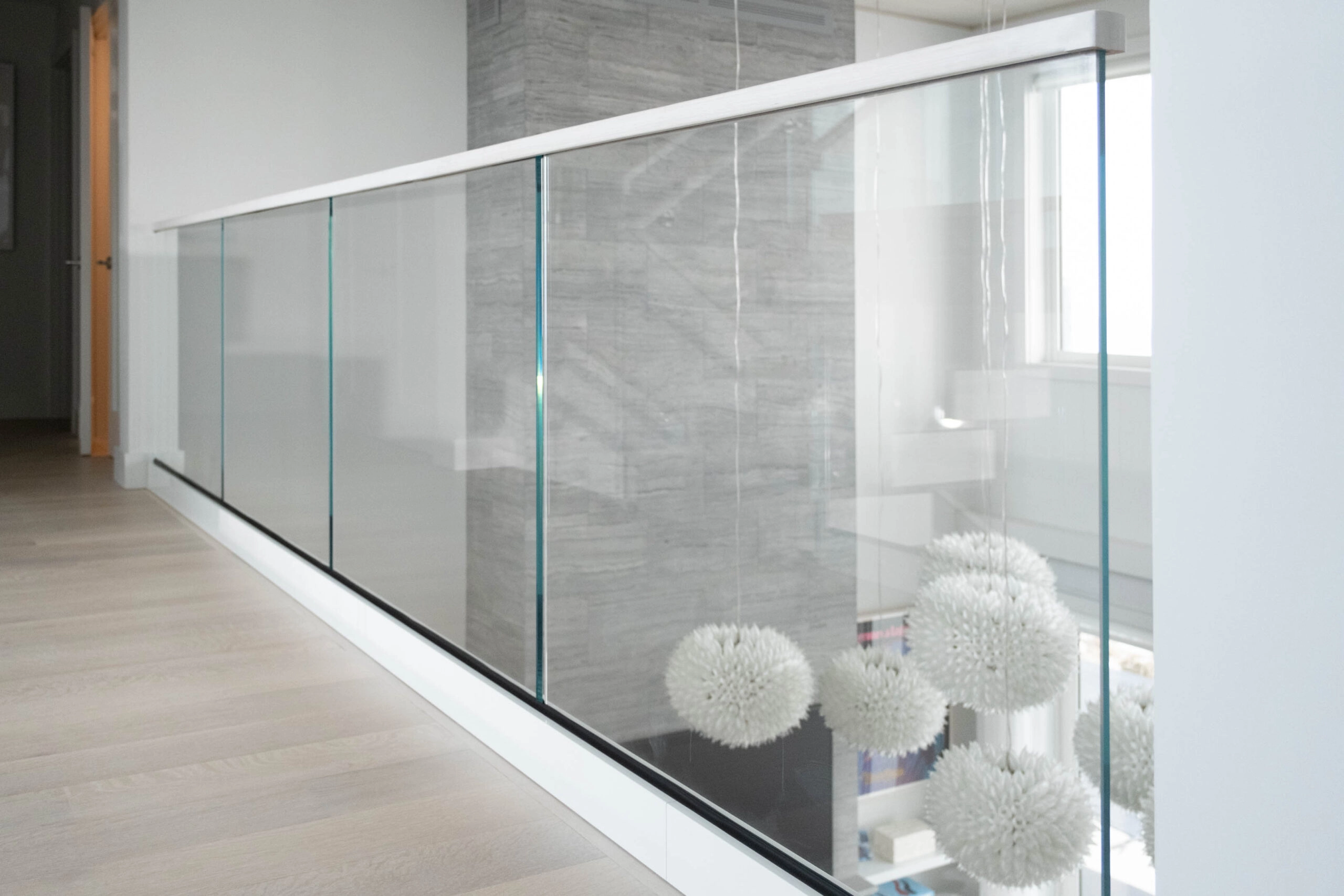 Balcony glass railing running past a stone-clad wall above plank flooring
