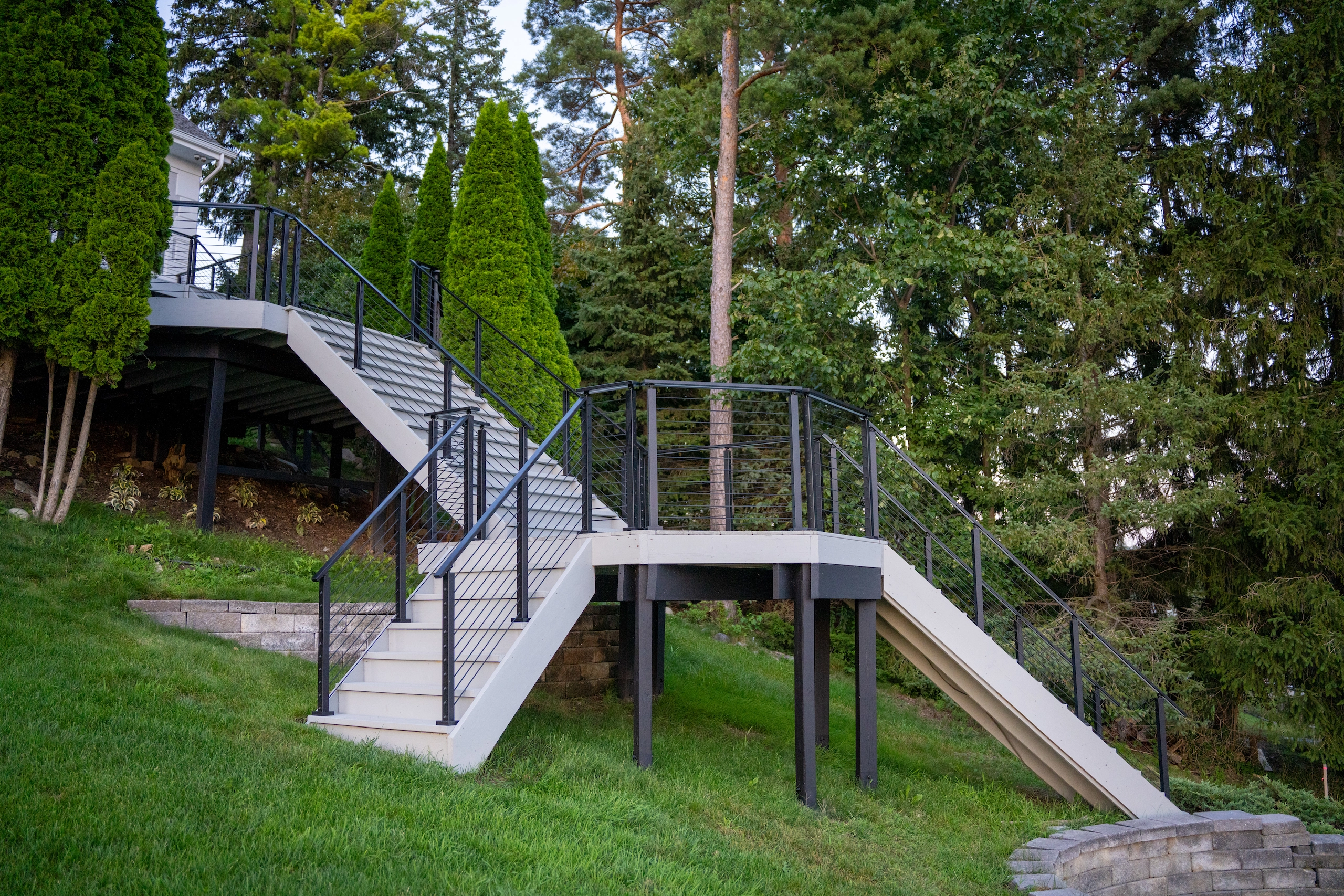 Elevated outdoor stair and landing framed in black railing on a wooded slope
