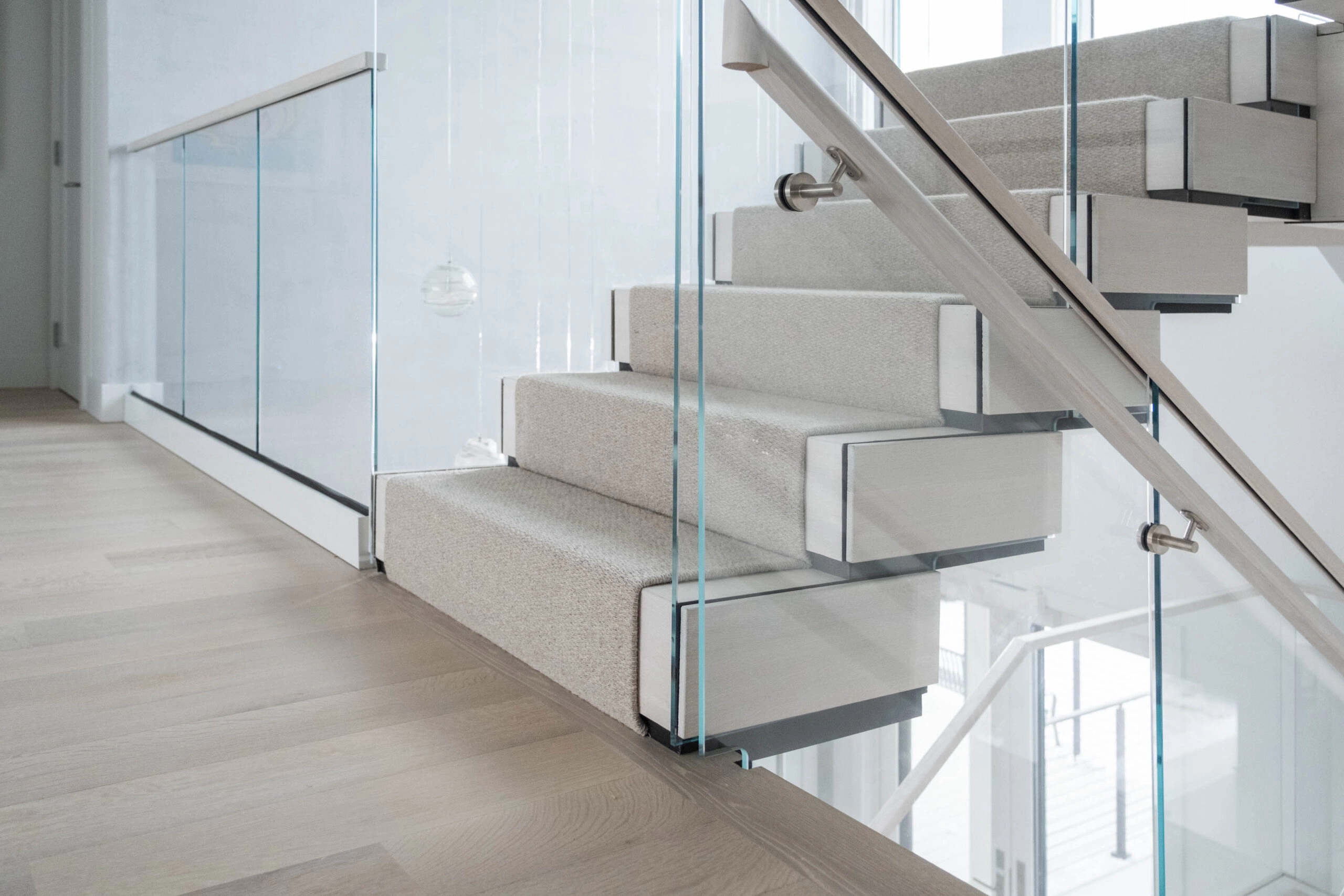 Base of the stair with carpeted treads, glass panels and slim metal handrail