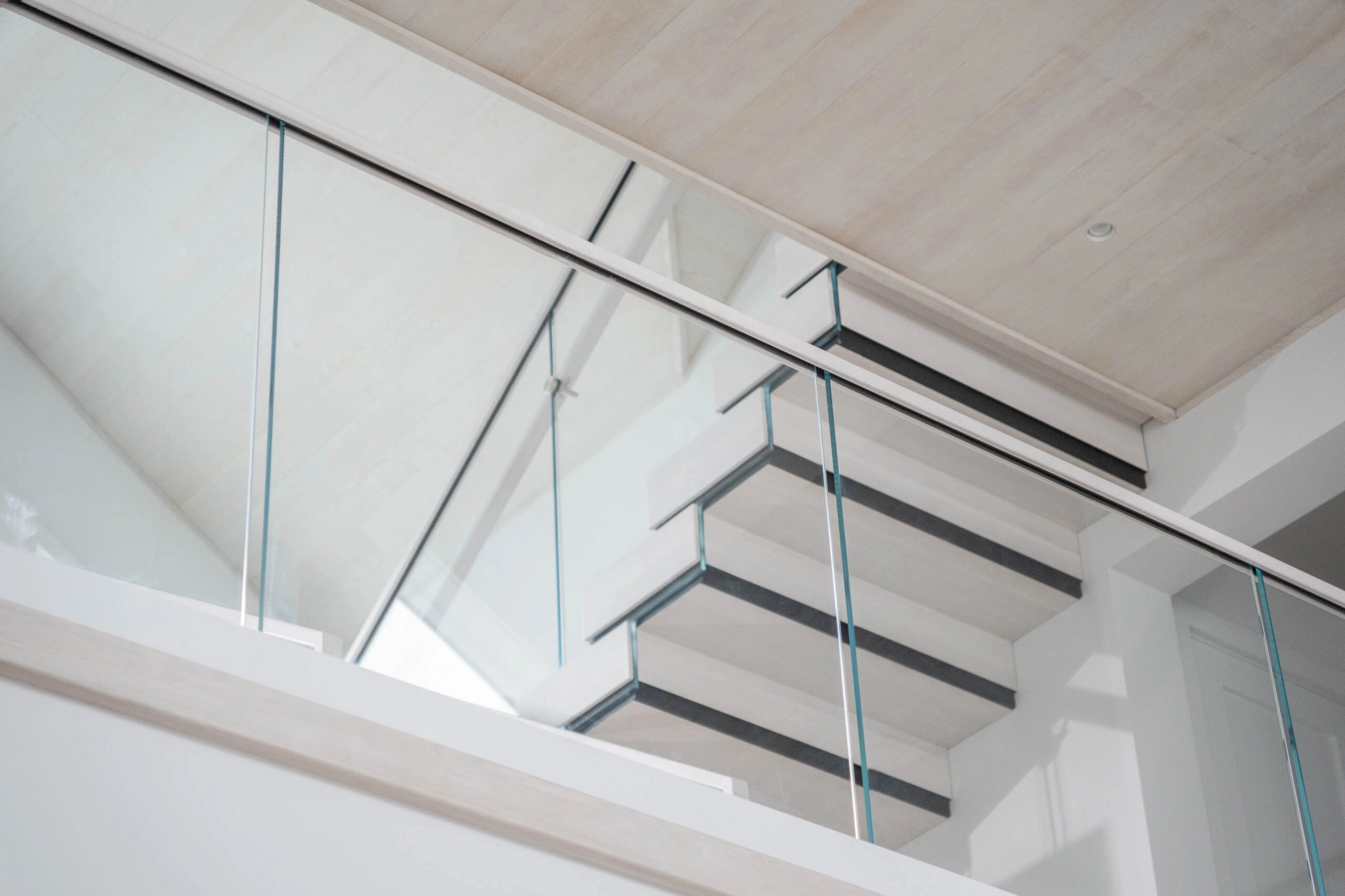 Looking up at the stack treads and glass railing beneath a wood-clad ceiling