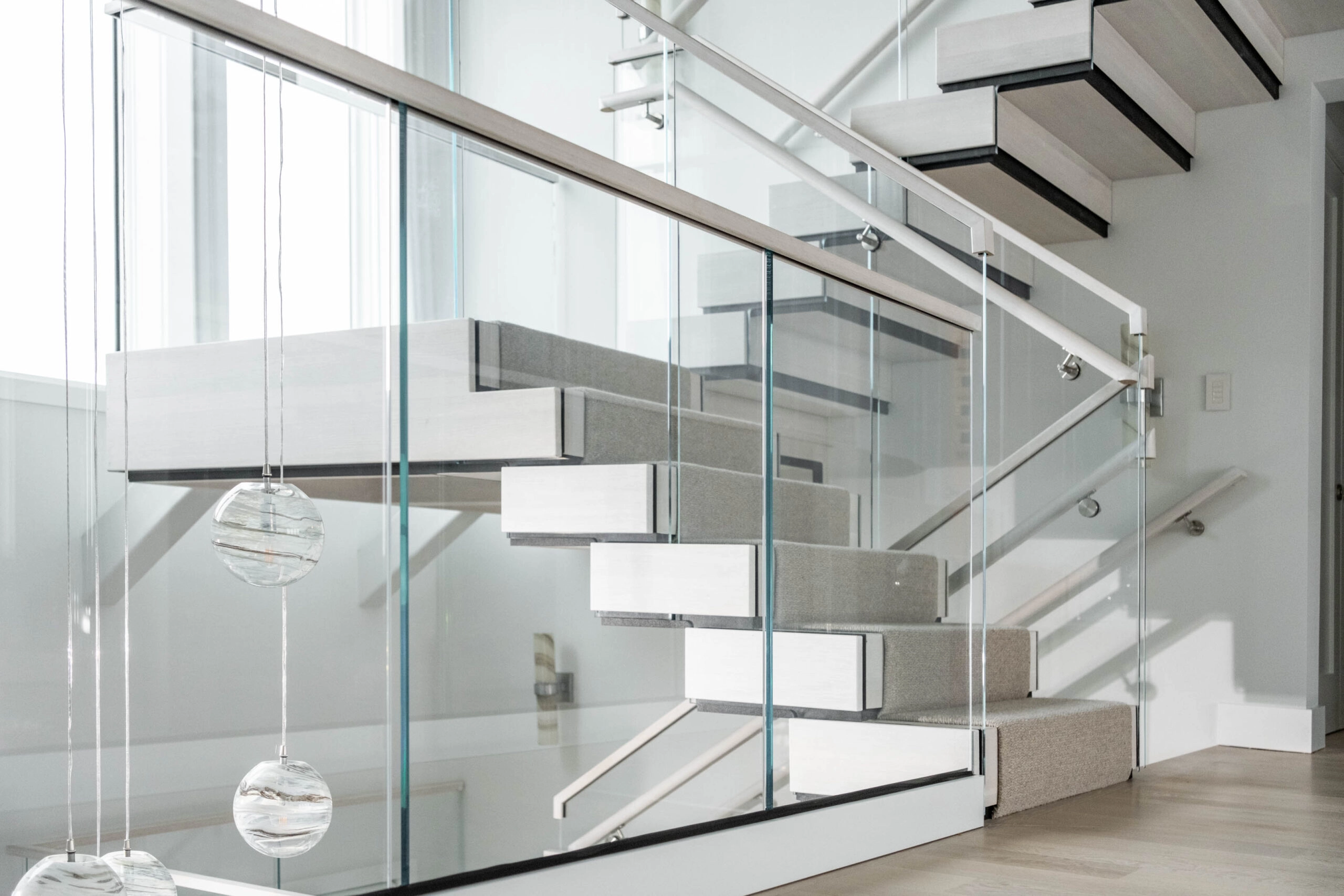 Side view of the stair with glass railing and hanging glass globe pendants