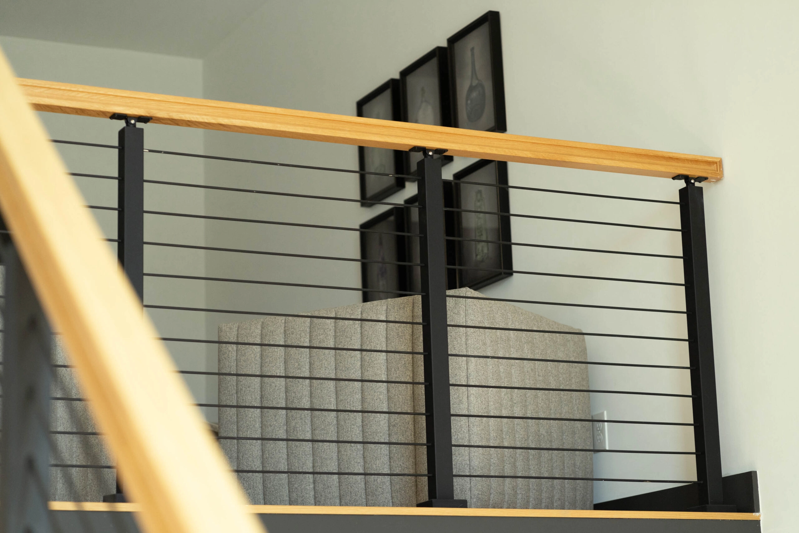 Balcony rod railing and wood handrail with framed art and seating behind