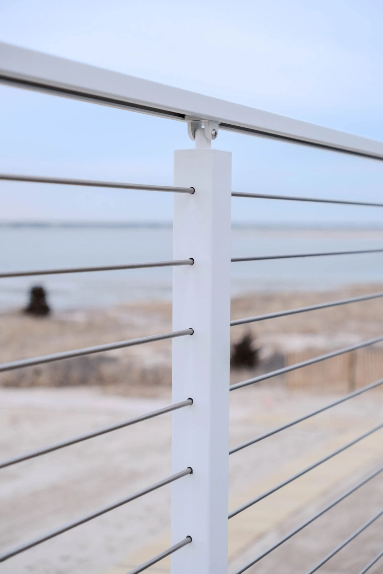 Close view of a white post threaded with stainless steel rods above the beach