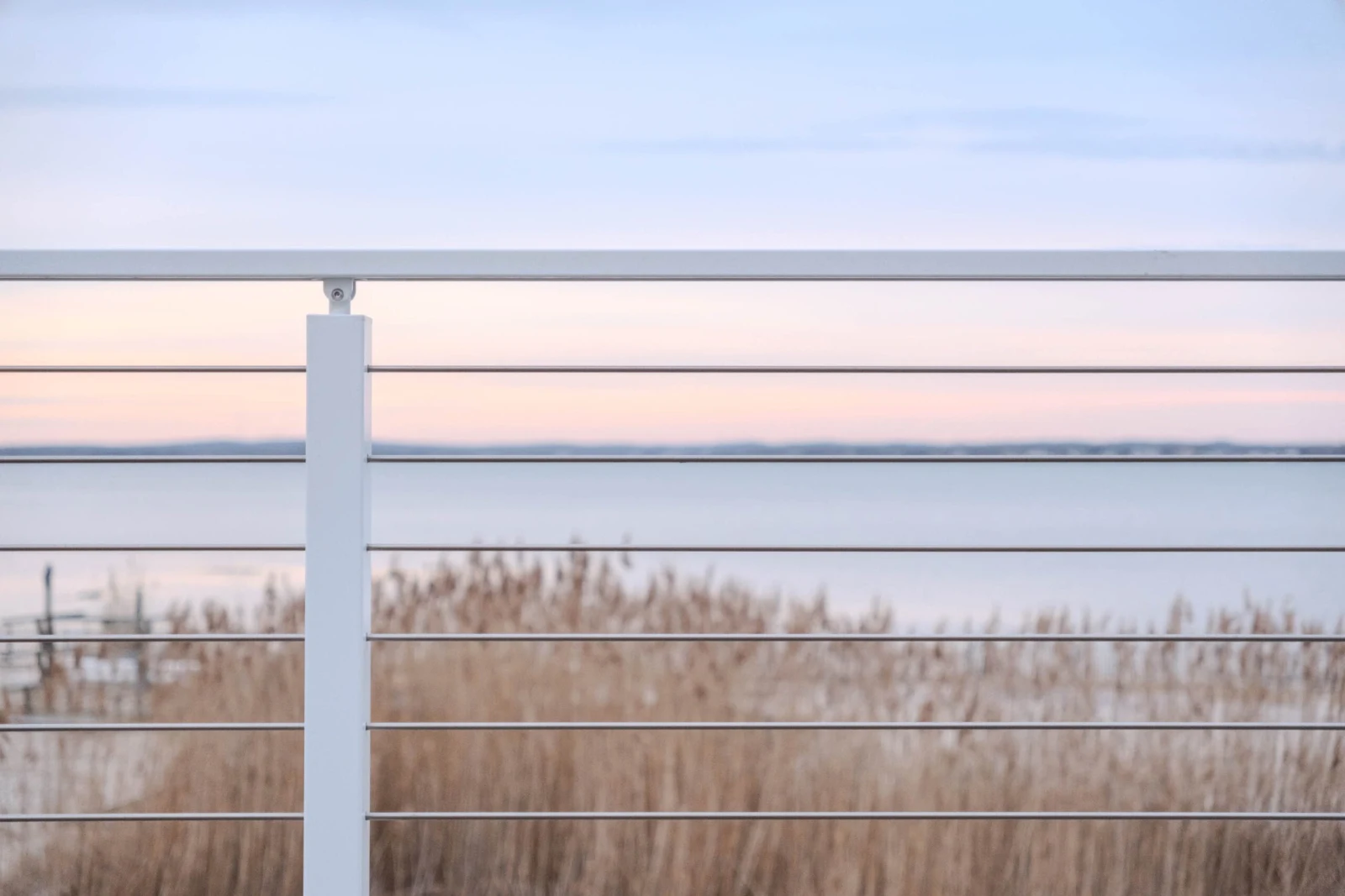 White top rail and level rods across dune grass with the bay at dusk