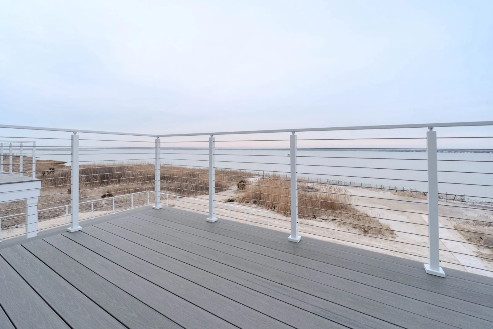 Corner of a gray deck wrapped in white rod railing facing open water