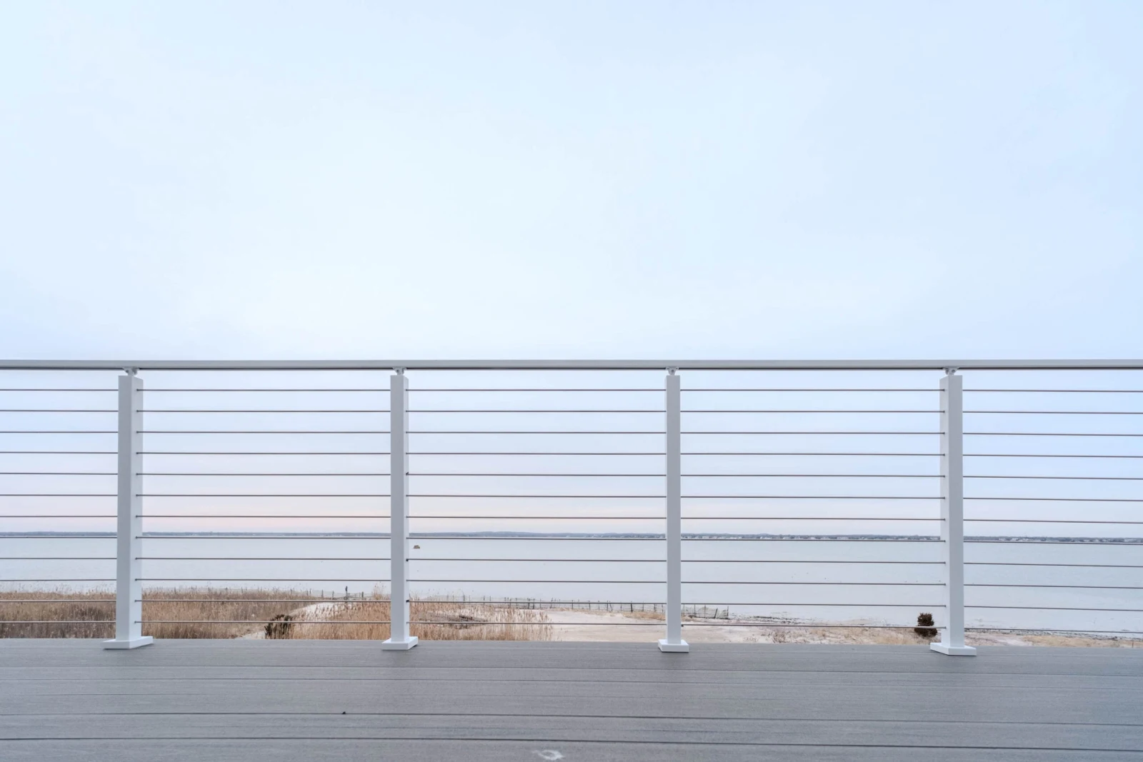 Four white posts spaced along the railing above the beach and calm bay