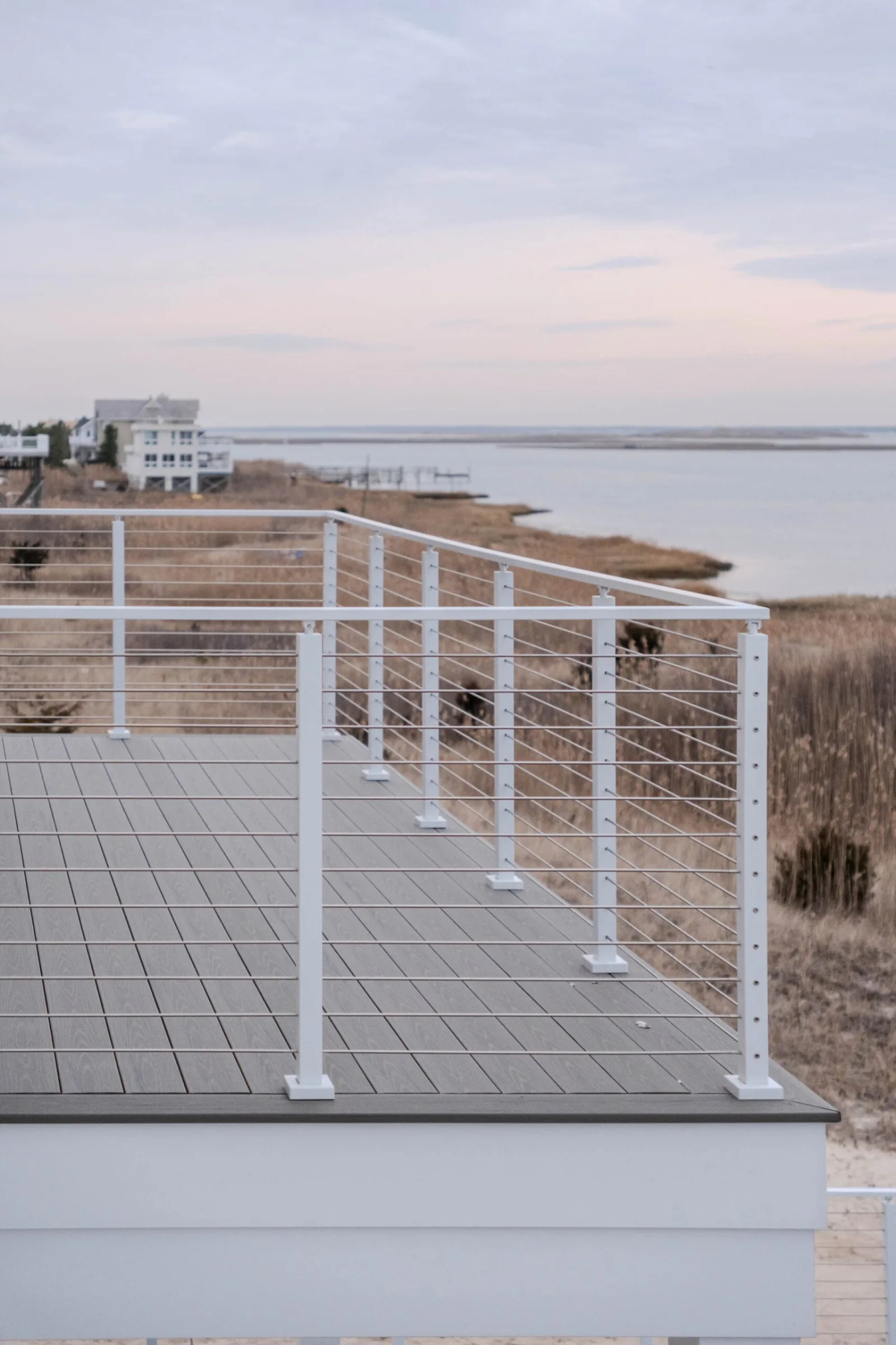 Deck railing with neighboring houses and dune grass across the inlet