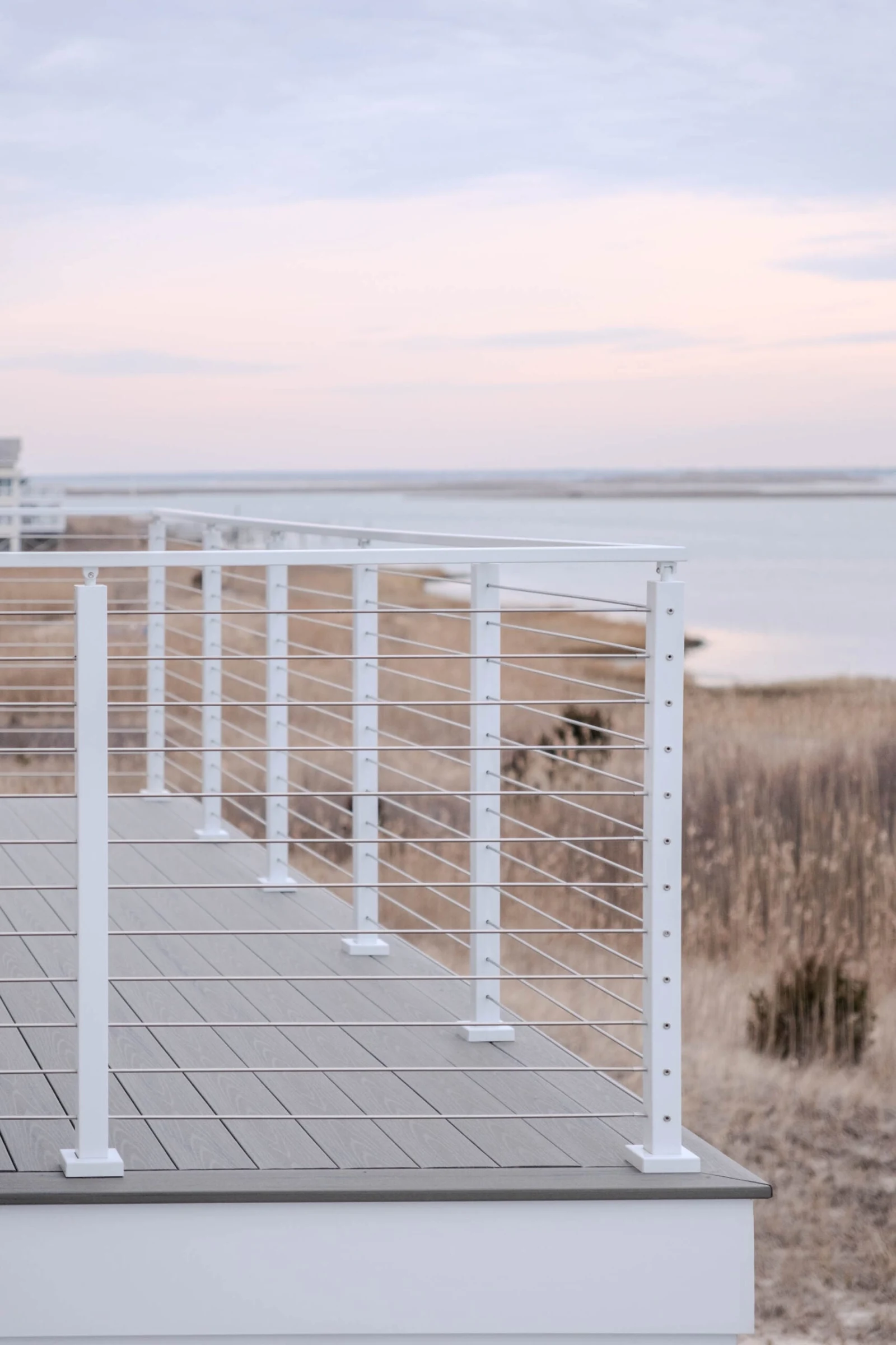 Deck corner railing seen from outside above tall dune grass at dusk