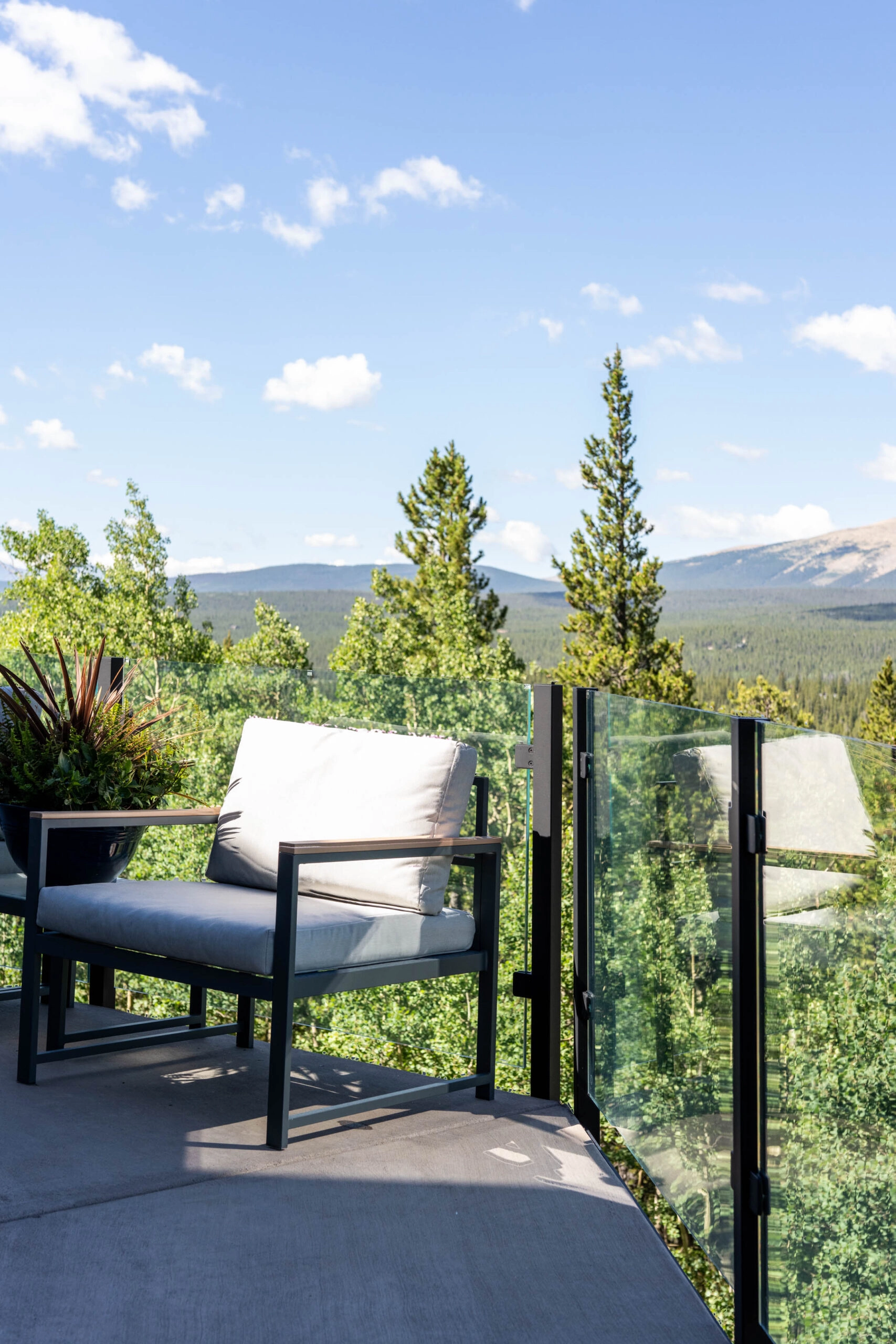 Lounge chair on a concrete deck beside frameless glass panels overlooking treetops