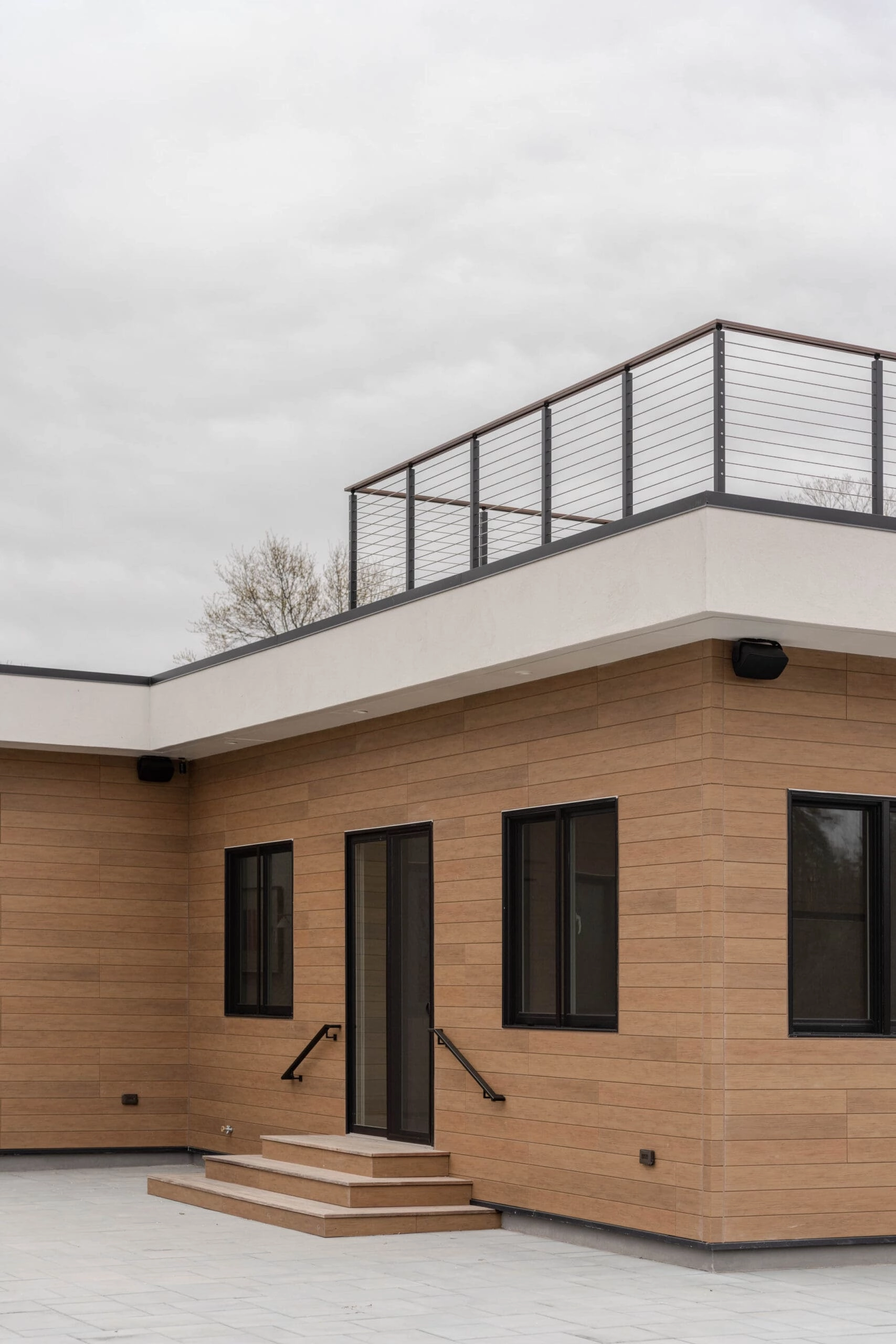 Wood-clad house corner with cable railing edging the roof deck above the entry steps