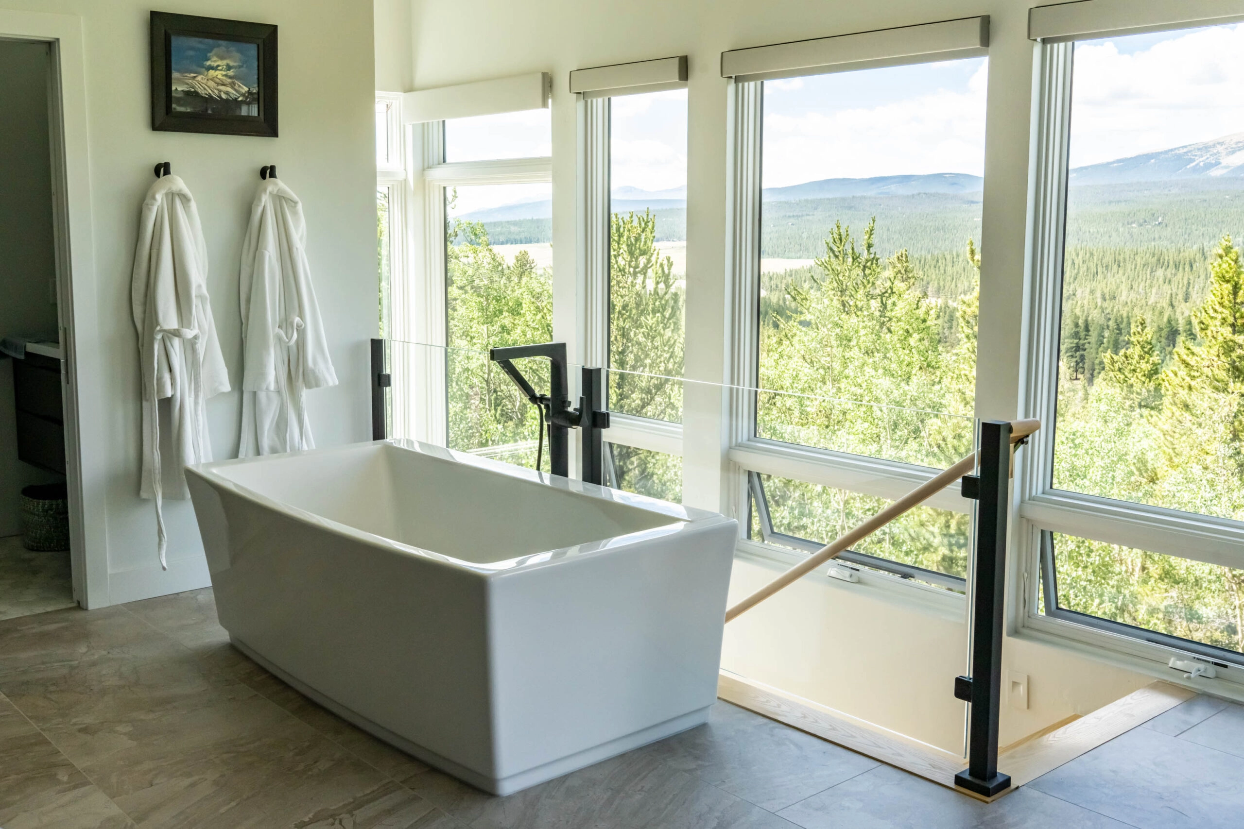 Freestanding tub by corner windows with a black railing post at the stair opening