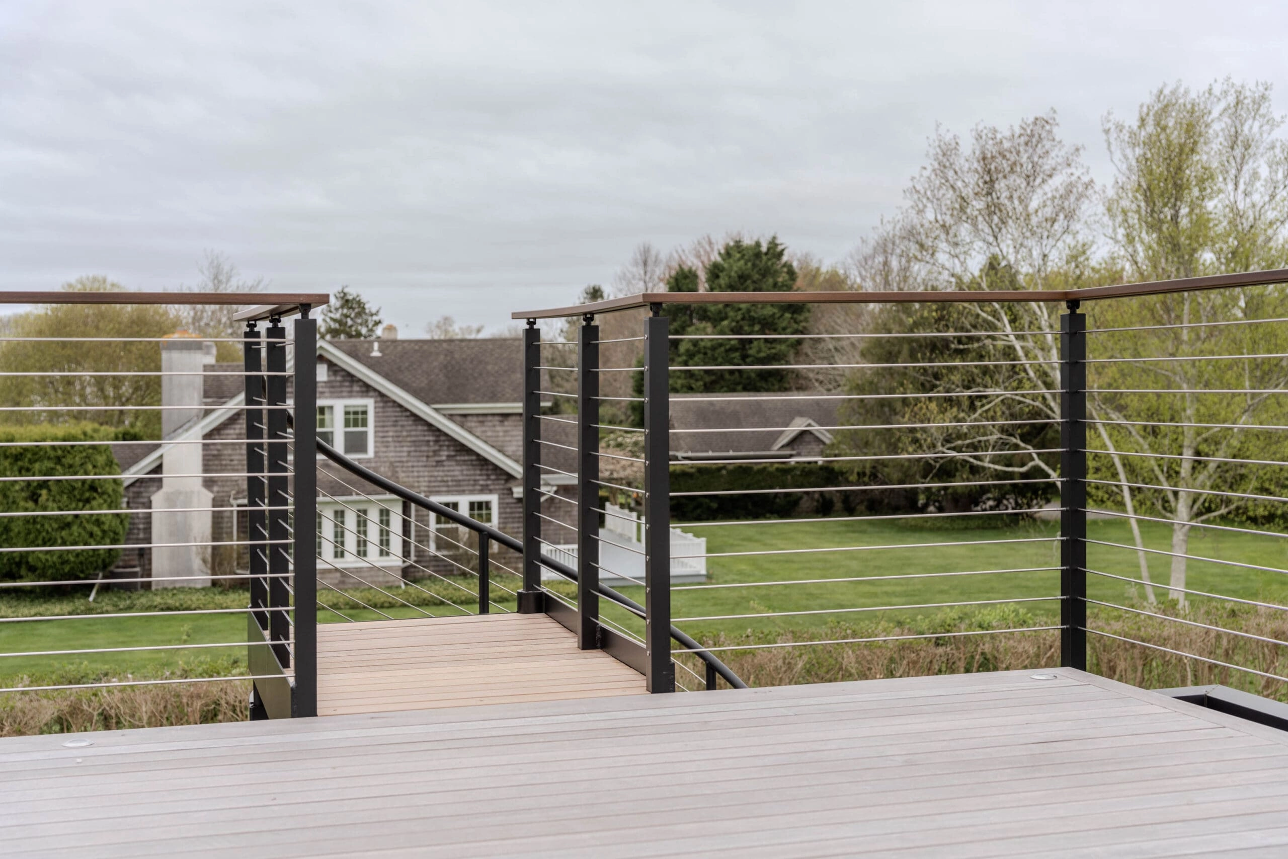 Wood-capped cable railing around a roof deck with steps down to the yard