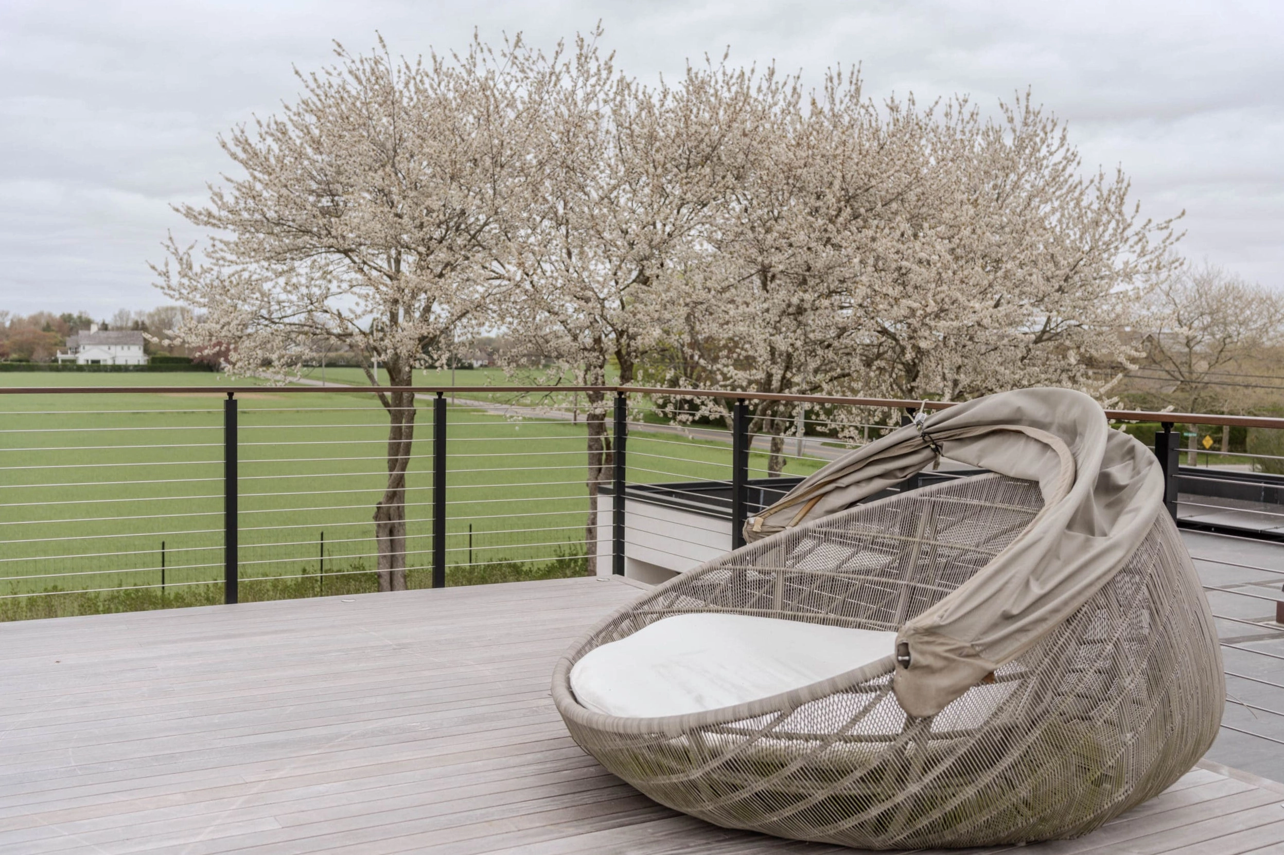 Woven daybed on a roof deck enclosed by black posts and horizontal cables