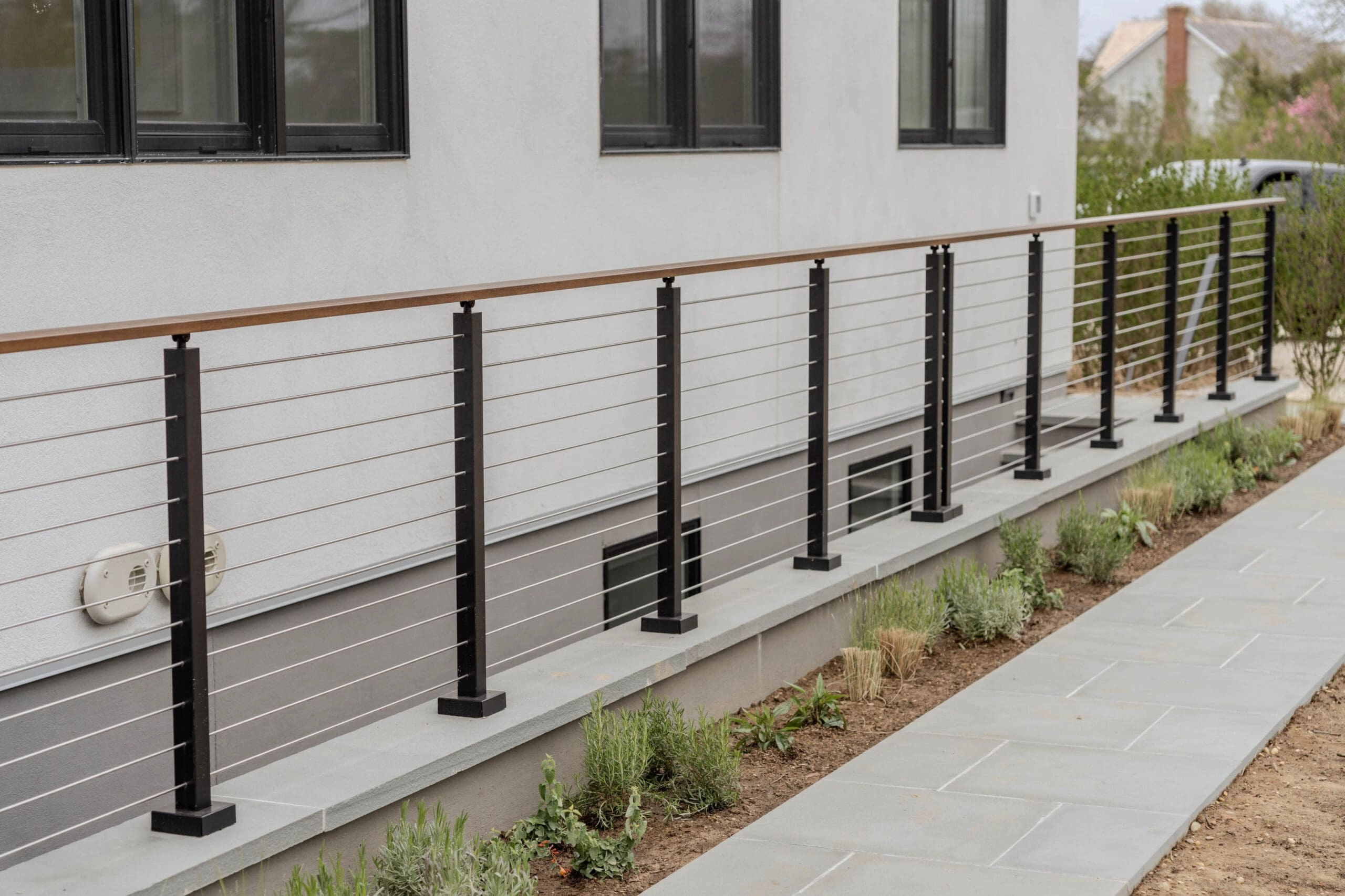 Ground-level cable railing running along a stucco wall beside a planted walkway