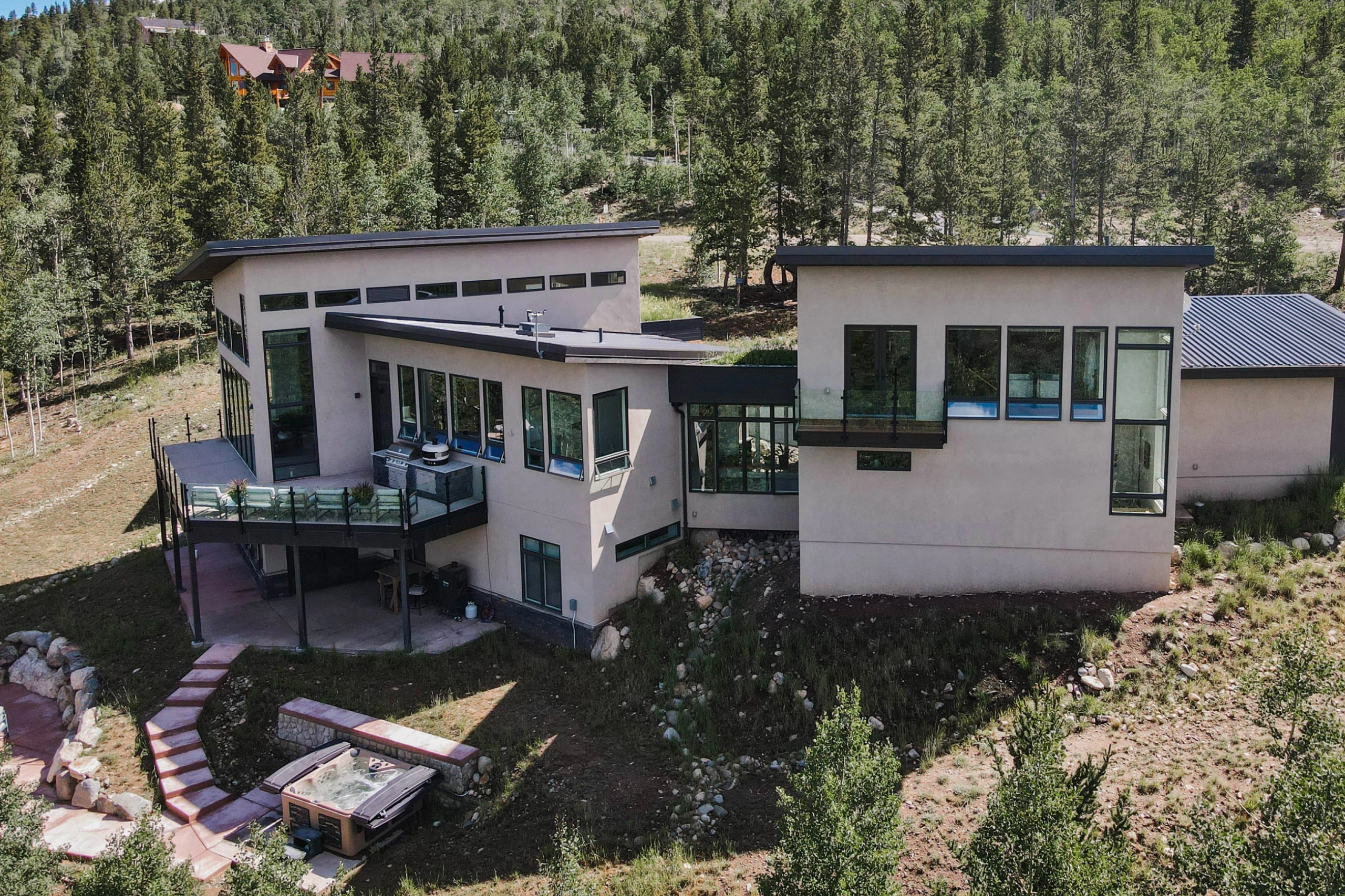 Aerial view of the hillside home and its glass-railed deck above a sloping yard