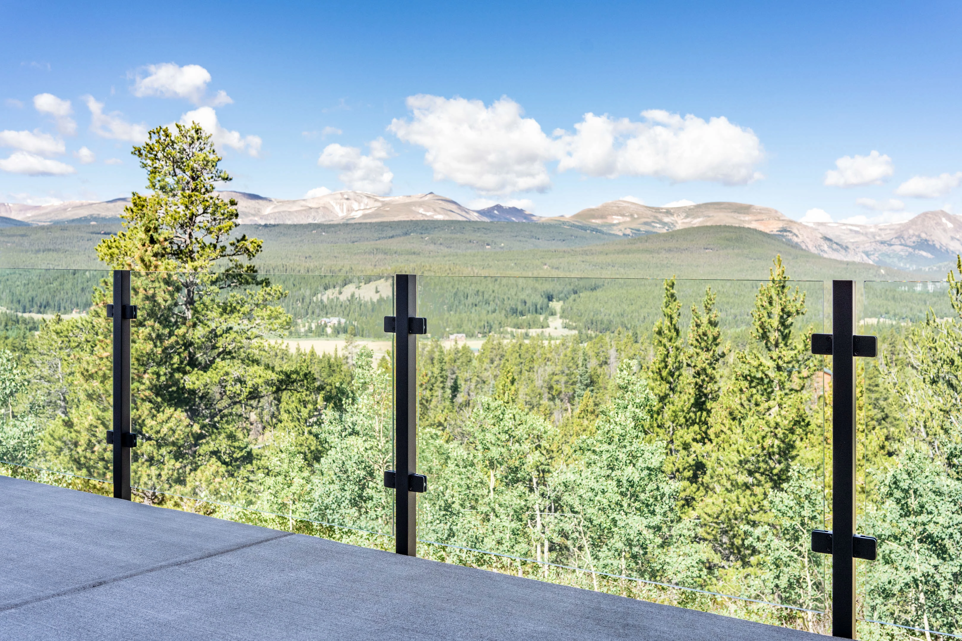 Glass railing posts lined along a rooftop deck with a wide forested valley view