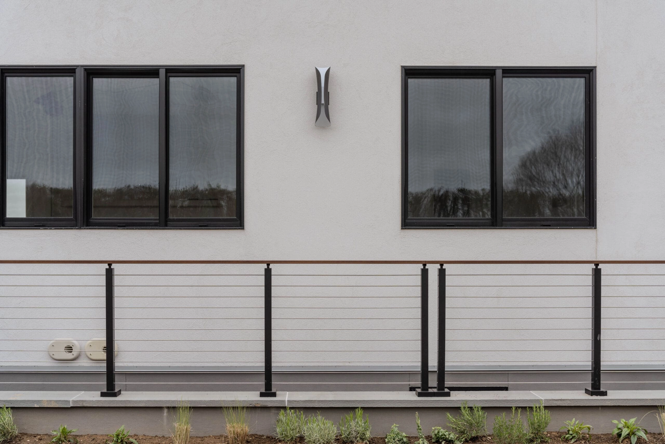 Low cable railing run below a row of black-framed windows on white stucco