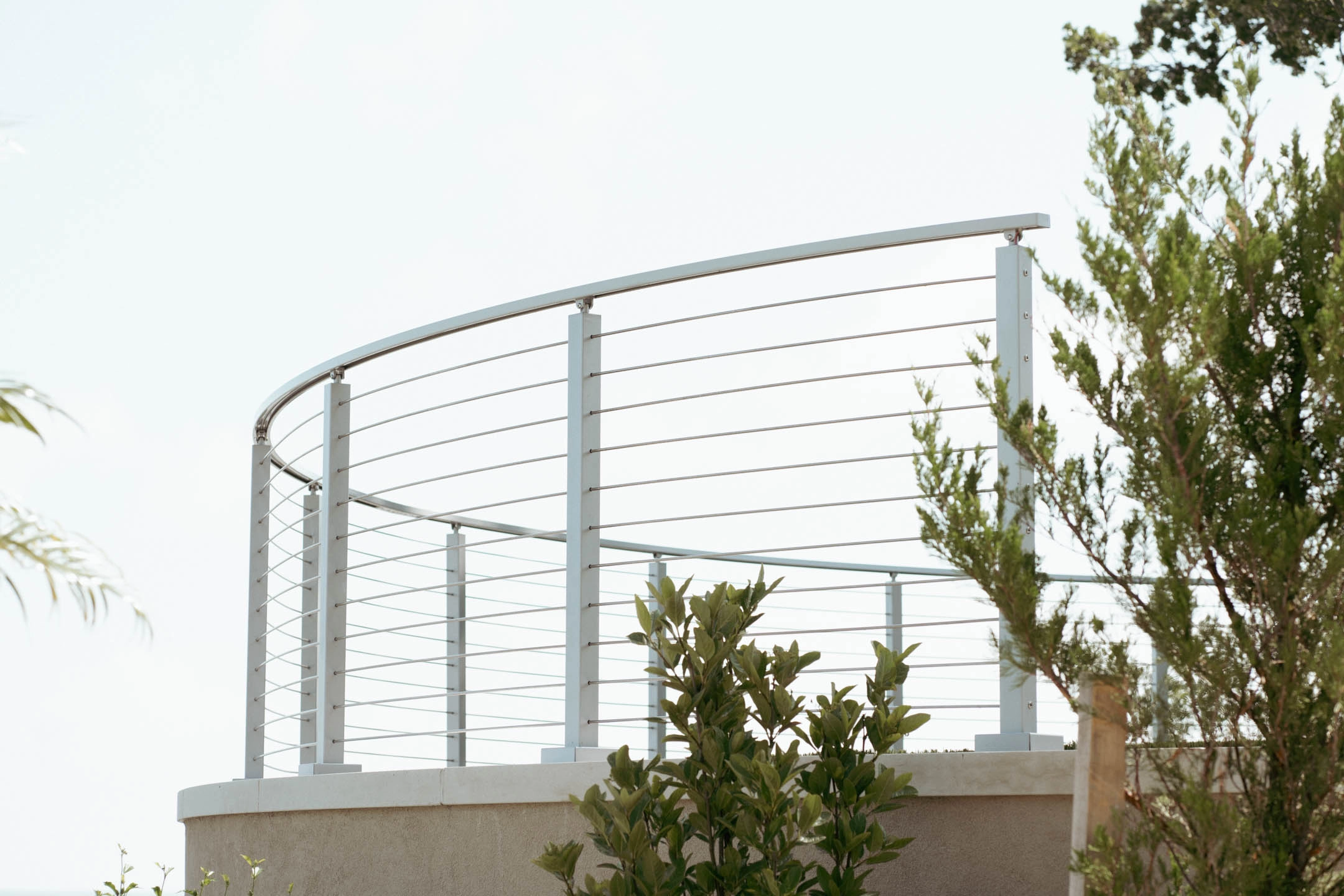 Curved run of silver posts and rods enclosing a raised terrace against the sky