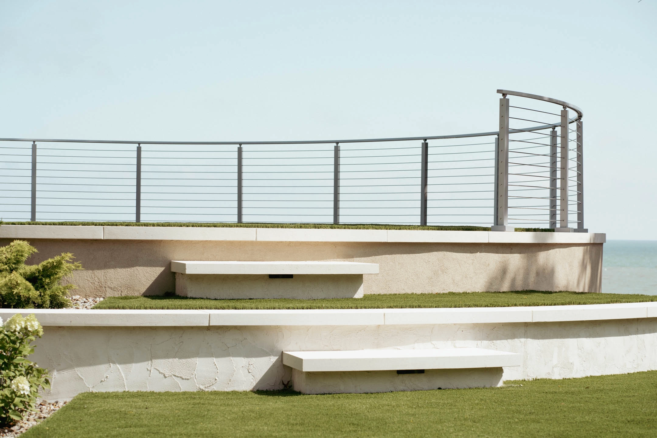 Long curved railing above a retaining wall with built-in benches on stepped lawns