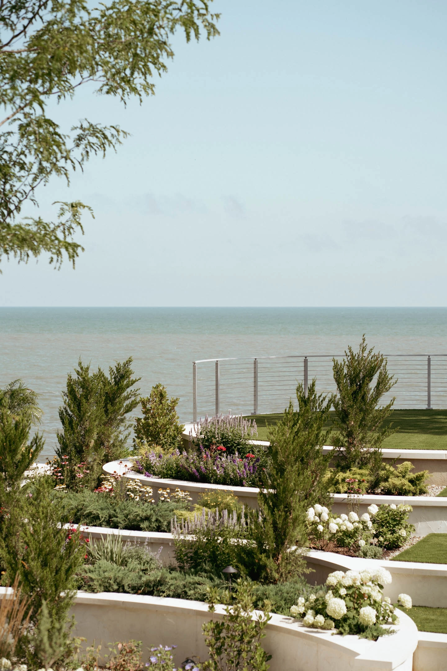 Layered garden terraces stepping down toward a rod railing and the water horizon