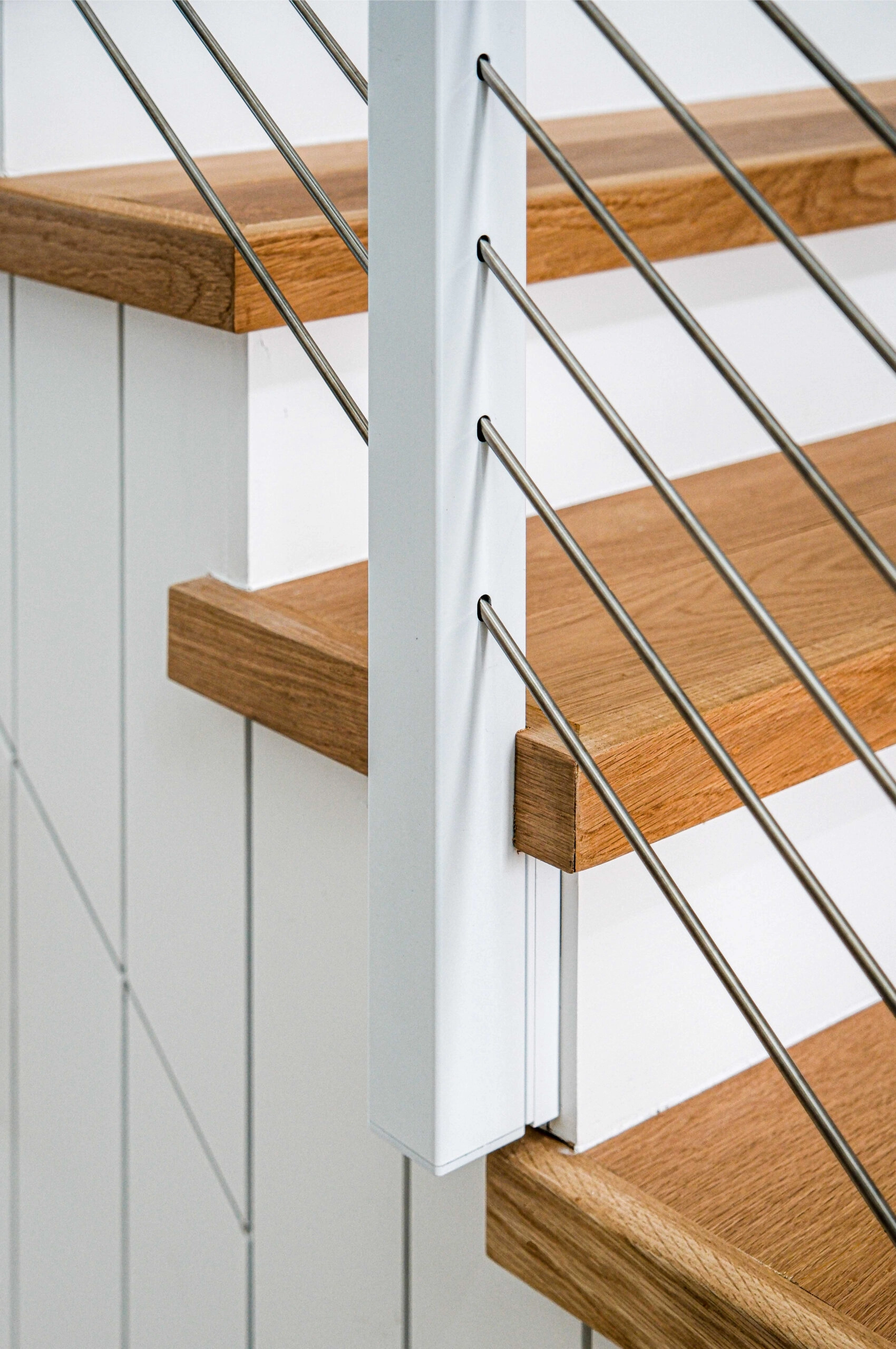 Close view of a white side-mount post with stainless rods beside a wood tread