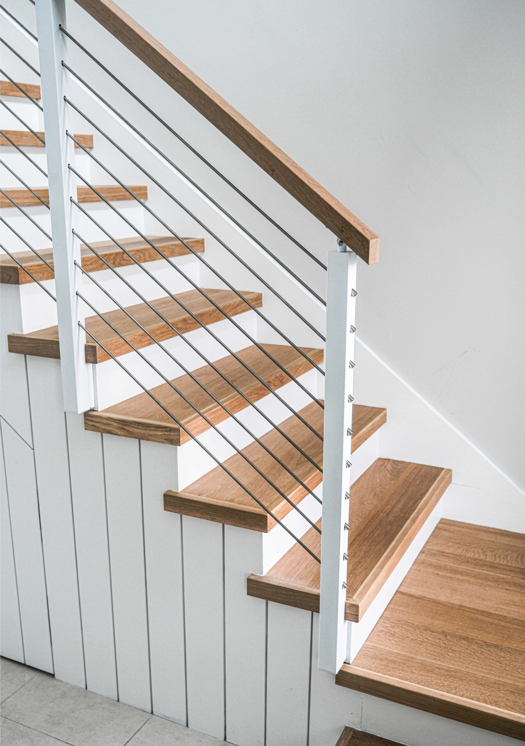 Looking down the stair at wood treads and white posts against a shiplap wall