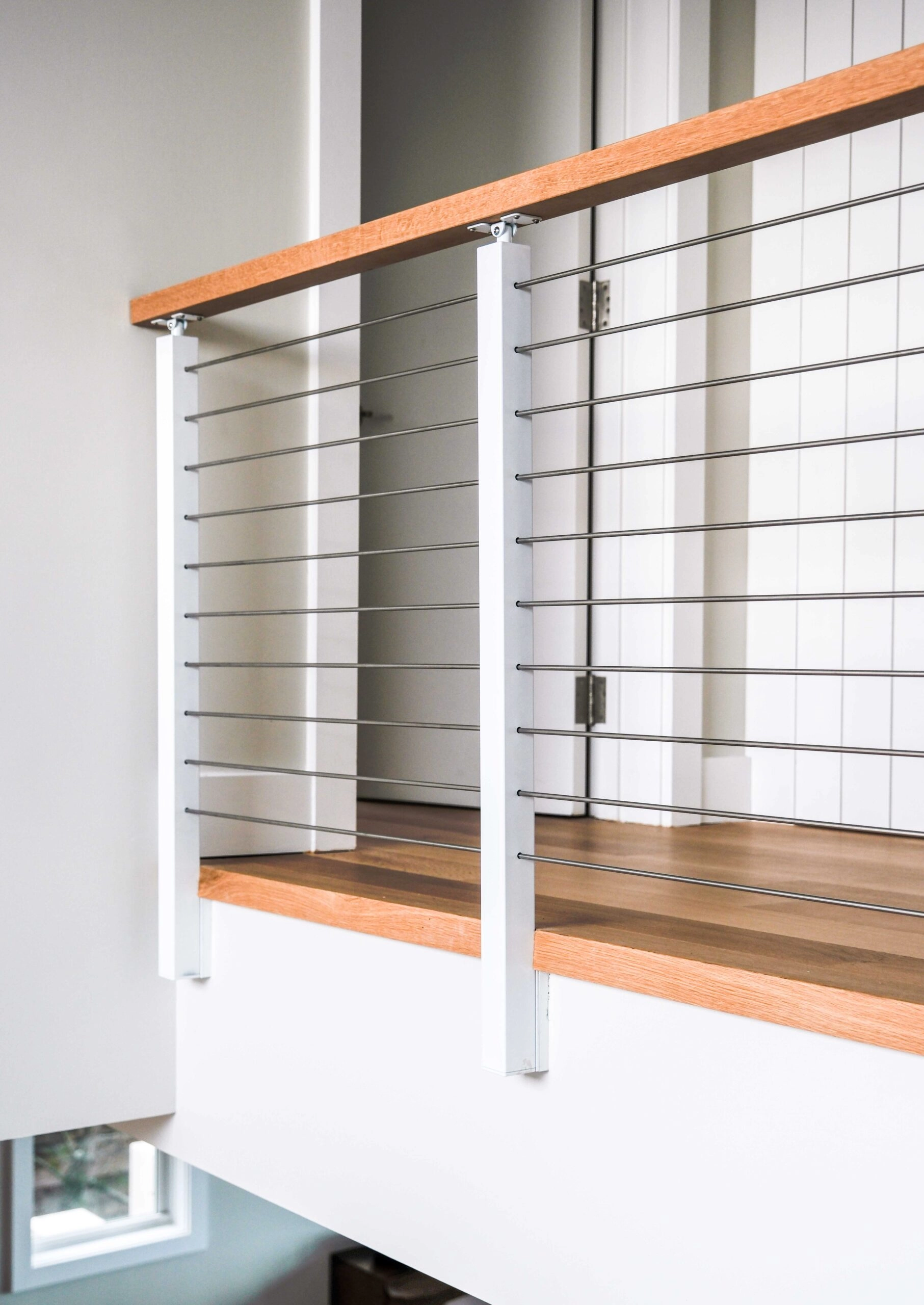 Landing railing of white posts and rods capped with a wood top rail