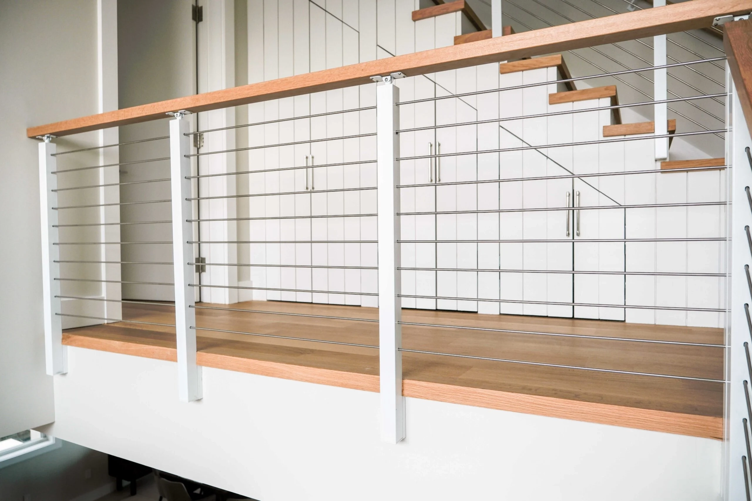 Railing run along the upper landing above wood flooring and white paneling