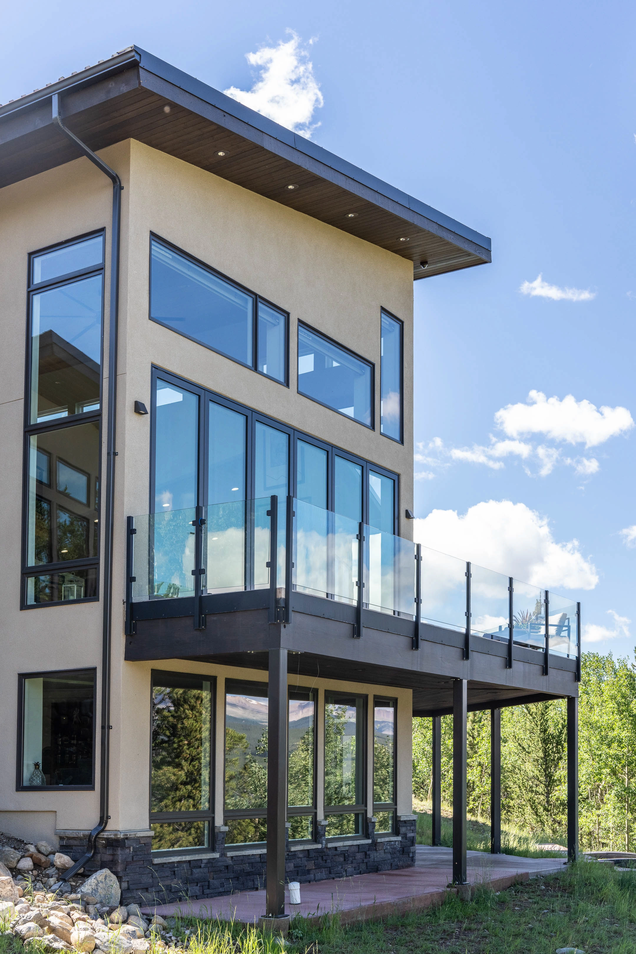 Glass in black posts fronts a raised deck on a stucco mountain home