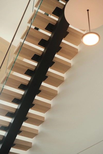 Wood treads step up a single black stringer past a hanging globe pendant.