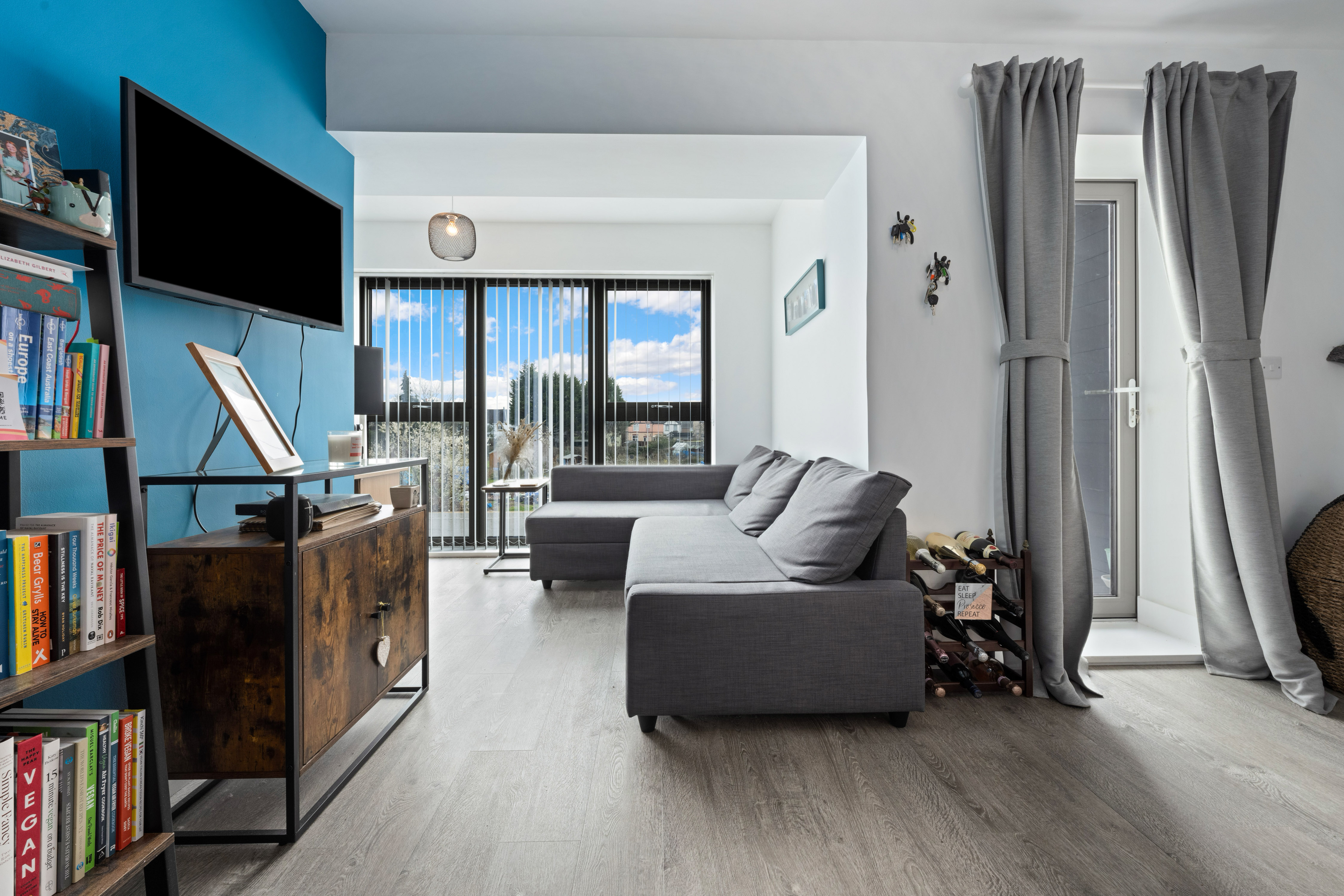 A modern bedroom with a white bed, wooden headboard, black lamp on a side table, and high windows